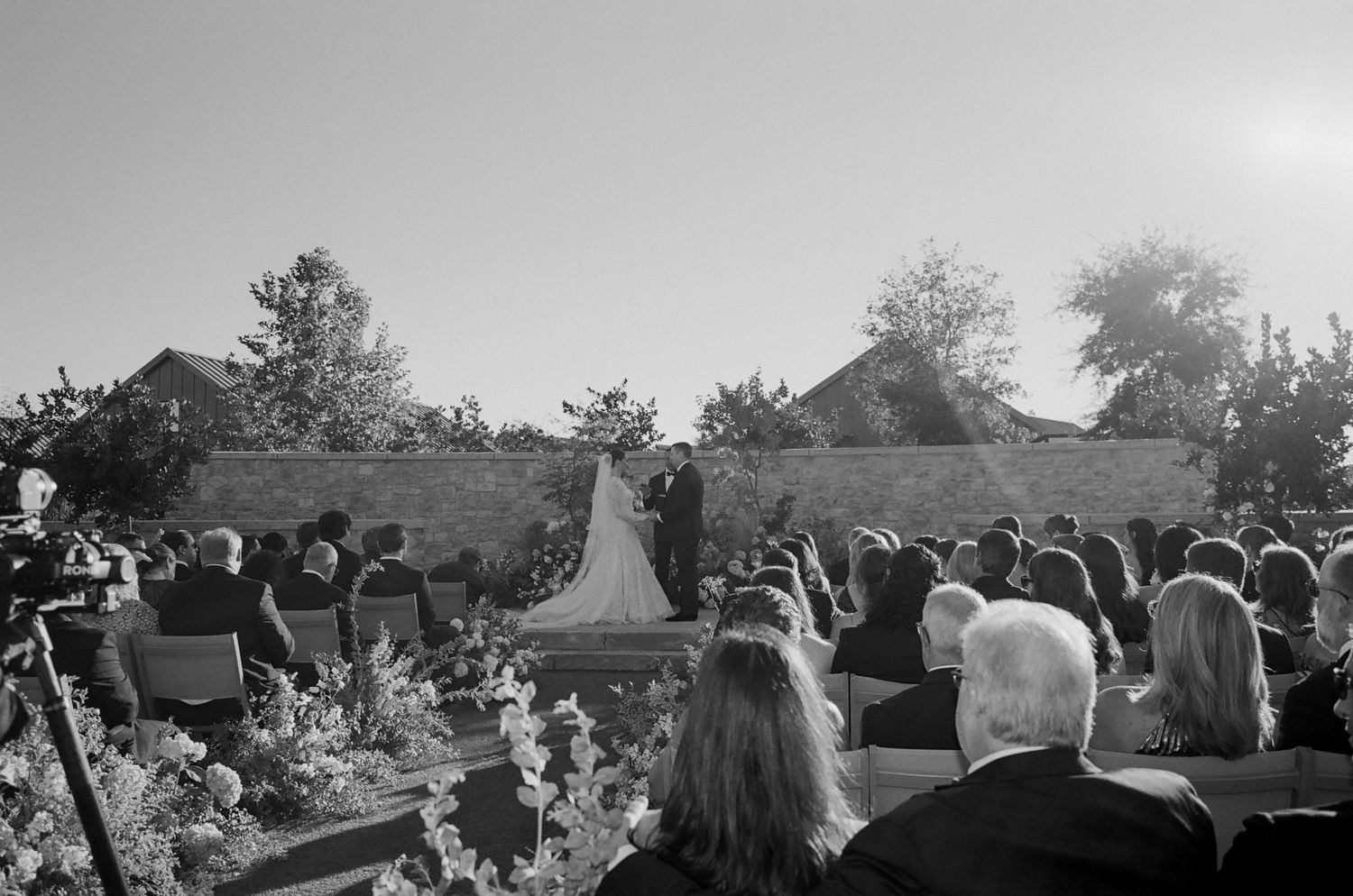 Guests seated outdoors at a wedding ceremony with trees and natural scenery in the background.