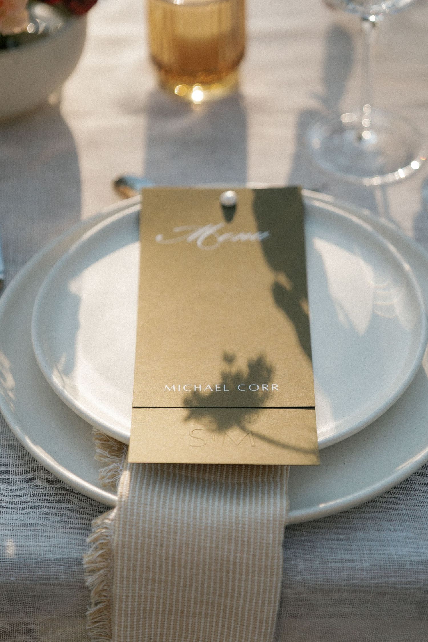 Elegant gold wedding menu card placed on white plate with grey napkin.