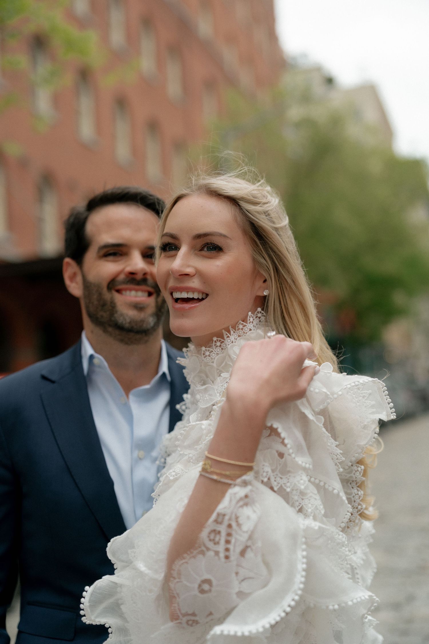 Romantic moment captured on a city street with white lace dress details and joyful expressions.