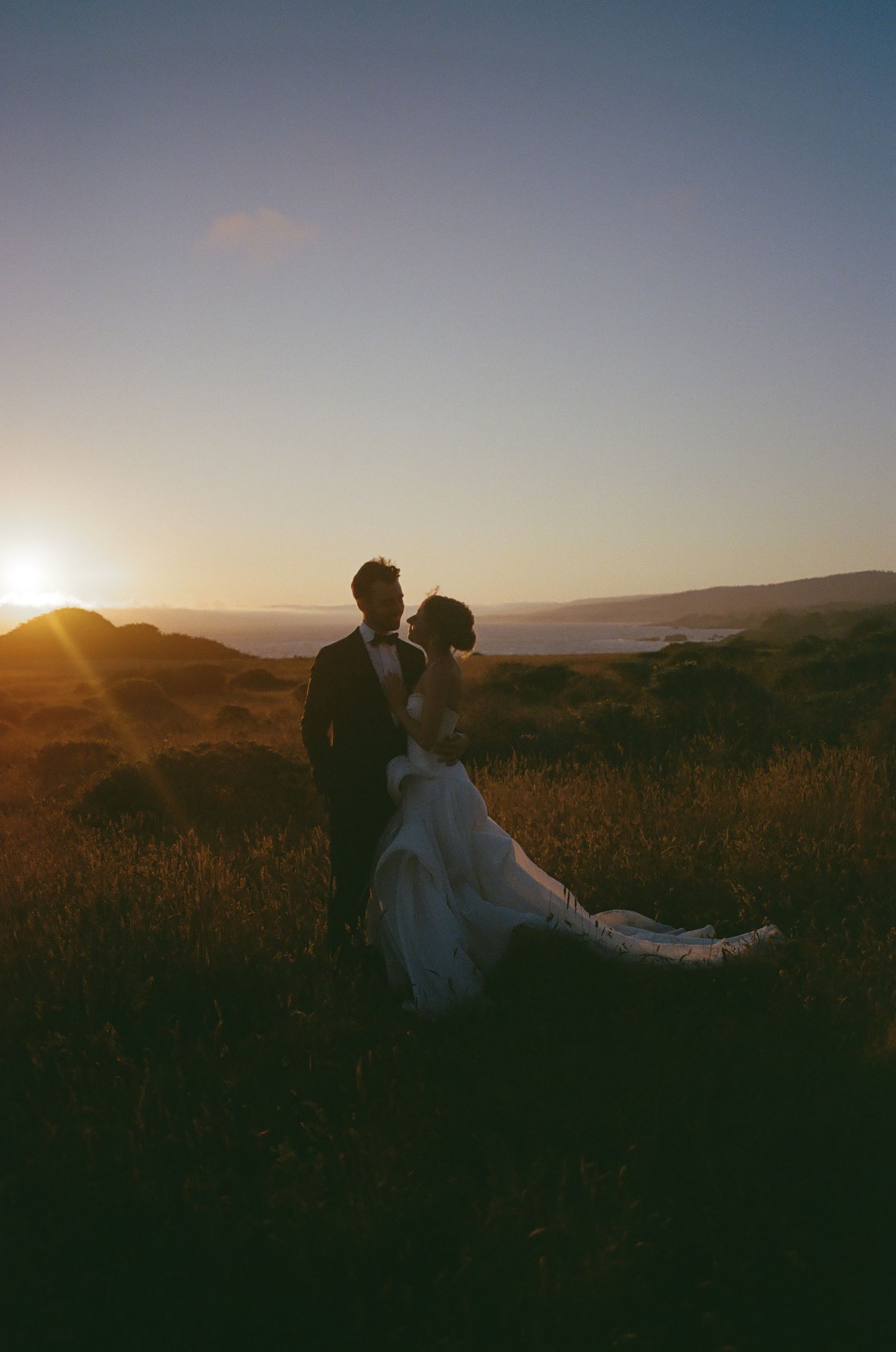 Couple sitting in a field during golden hour with mountains in the background.