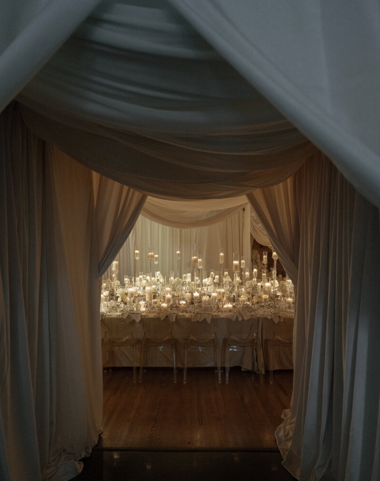 Elegant wedding reception venue with draped fabric ceiling and hanging crystal chandeliers creating a romantic atmosphere.