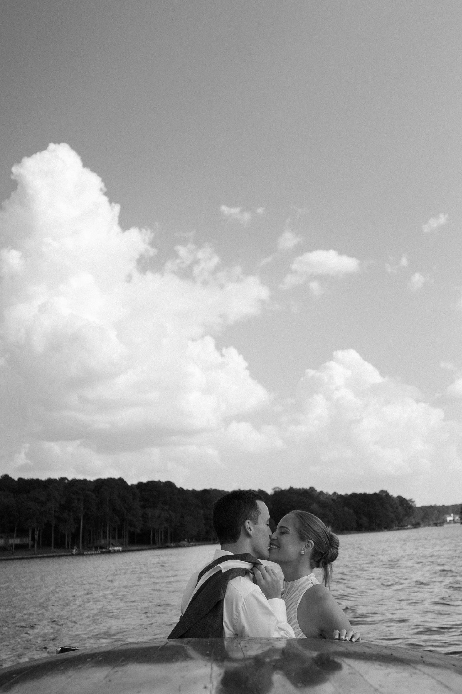 Black and white photo of a romantic moment on a boat against cloudy skies over water.