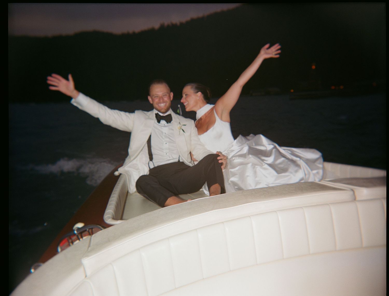 Couple celebrating with arms raised while sitting on a boat at dusk.