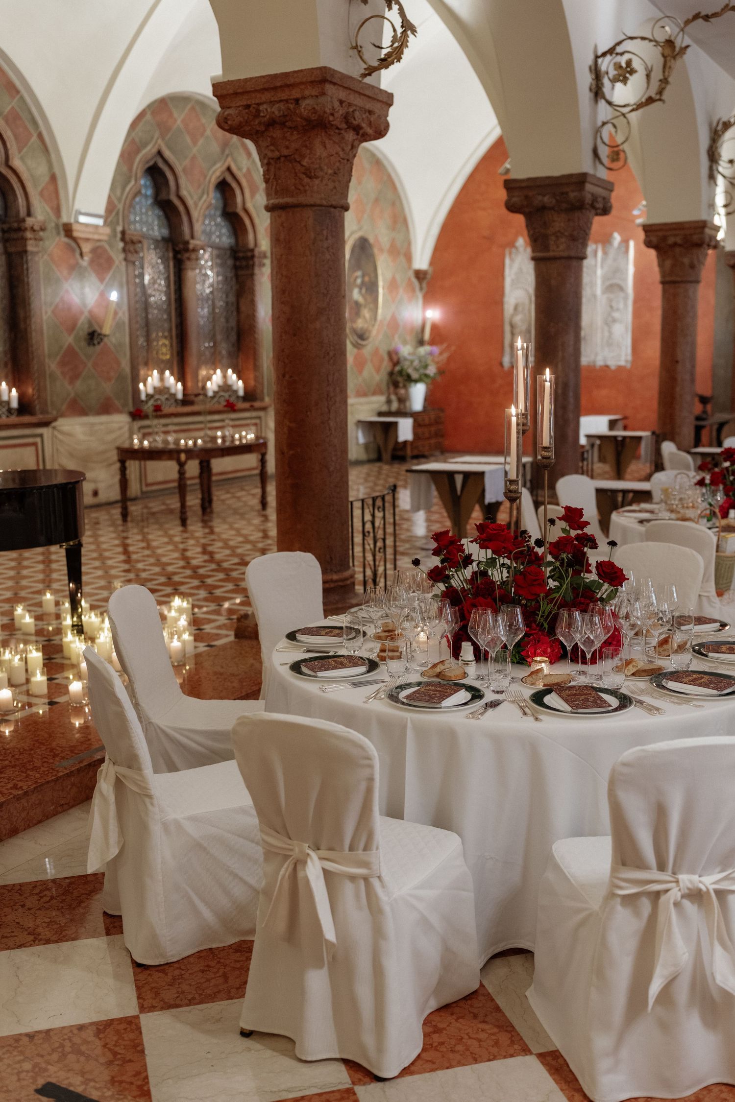 Elegant wedding reception in a historic venue with white chair covers, red rose centerpieces, and arched columns.