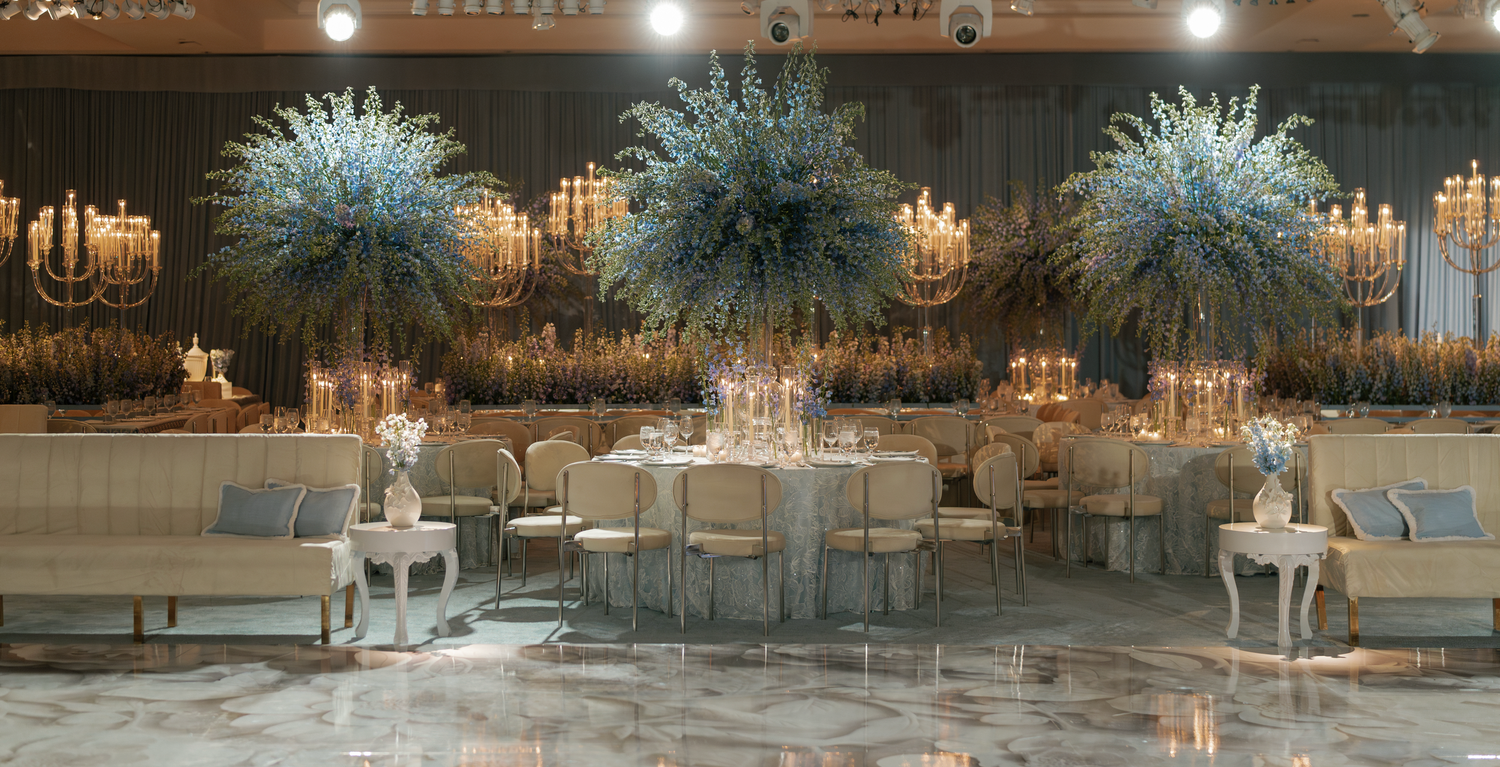 Elegant wedding reception venue with crystal chandeliers and blue floral centerpieces on white tablescapes. Luxury Wedding Reception.