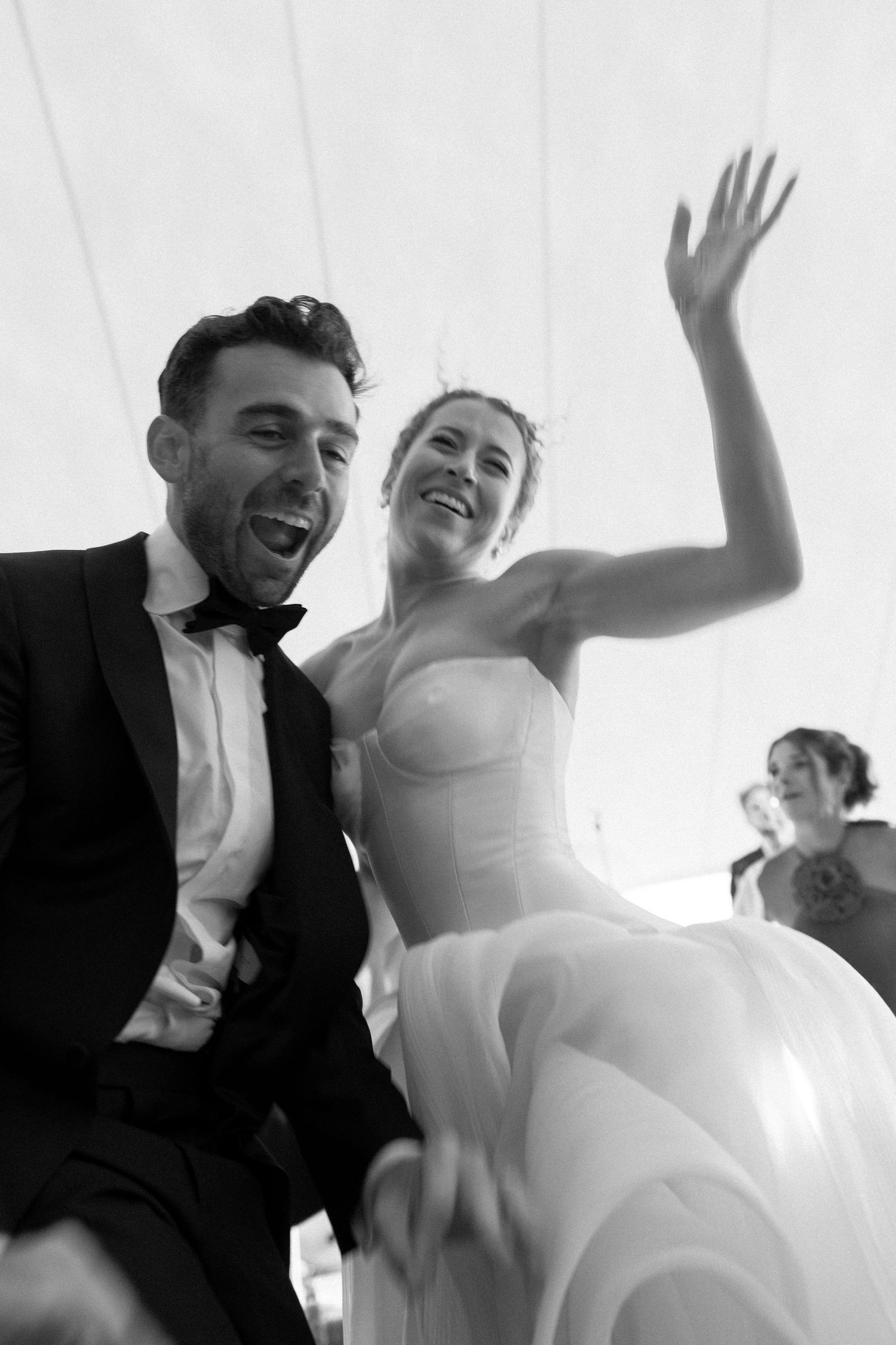 Joyful wedding celebration captured in black and white with flowing white dress and formal attire.