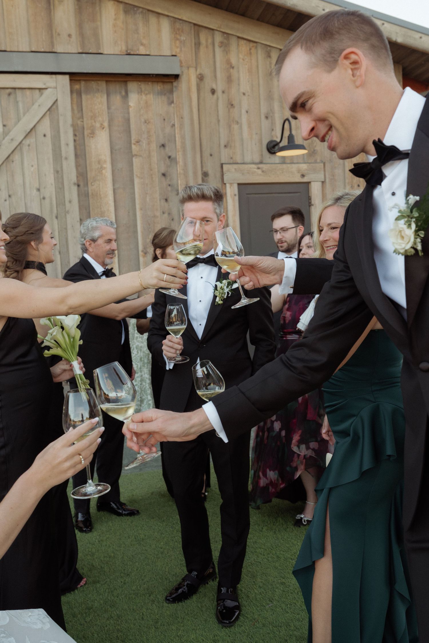 Wedding guests toast with champagne glasses outside a rustic barn venue.
