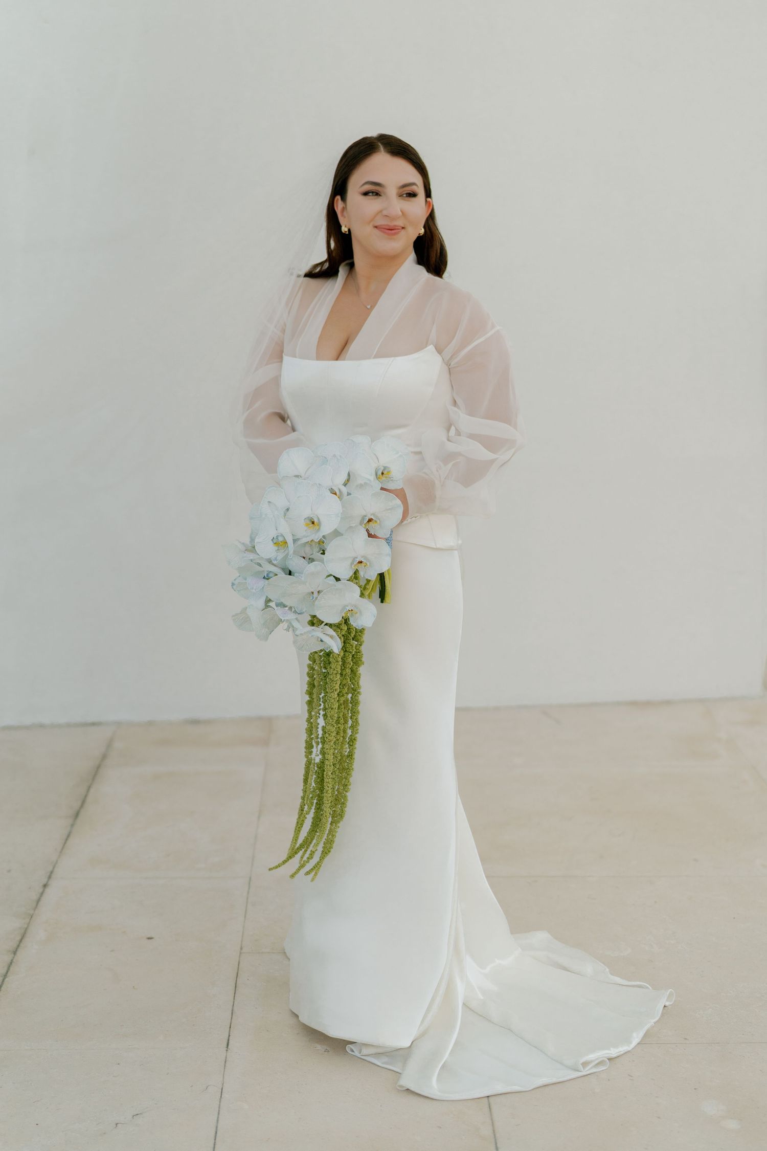 Bride in modern white wedding gown holding a cascading orchid bouquet.