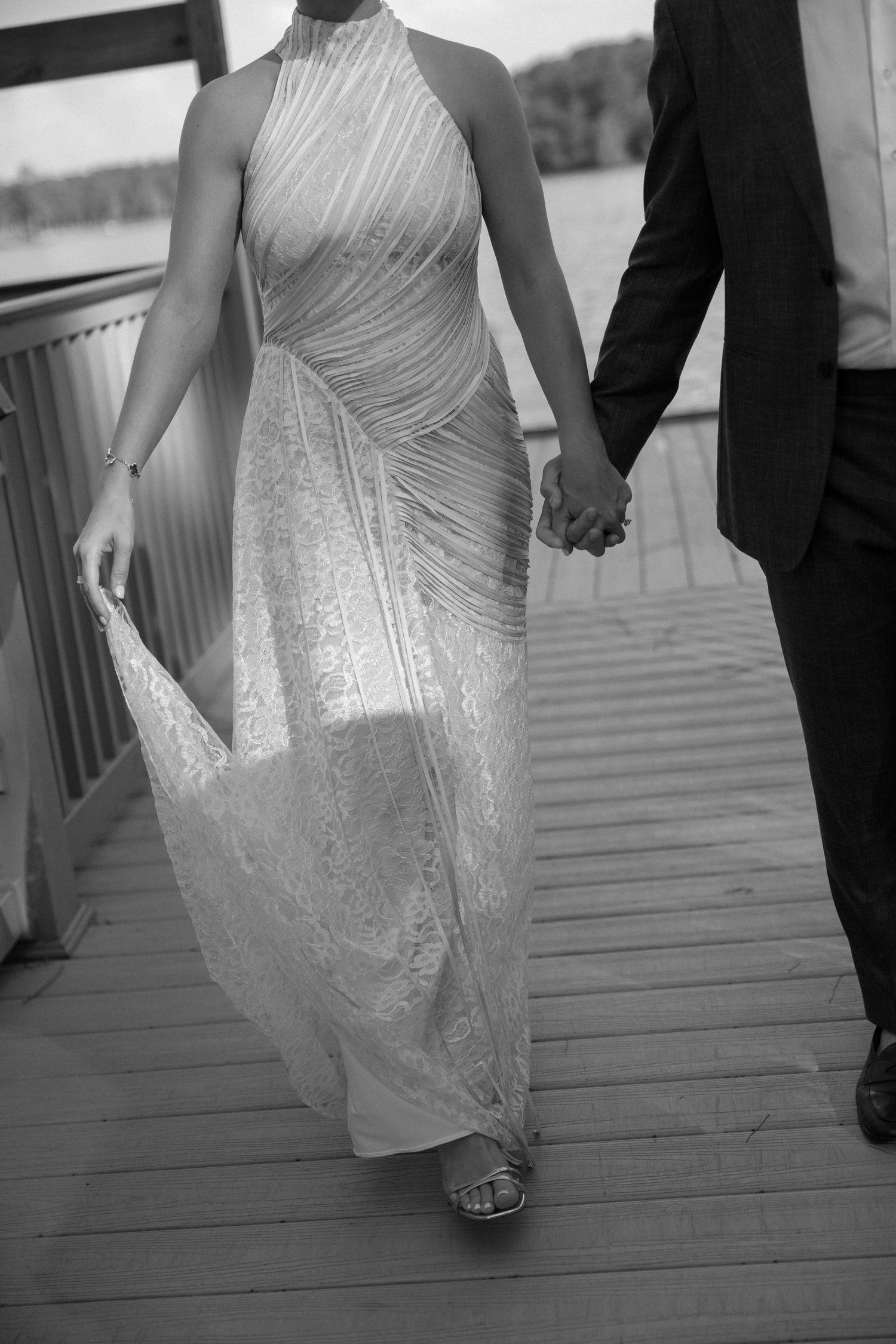 An elegant silver halter dress flows as a couple walks hand-in-hand on a wooden deck.