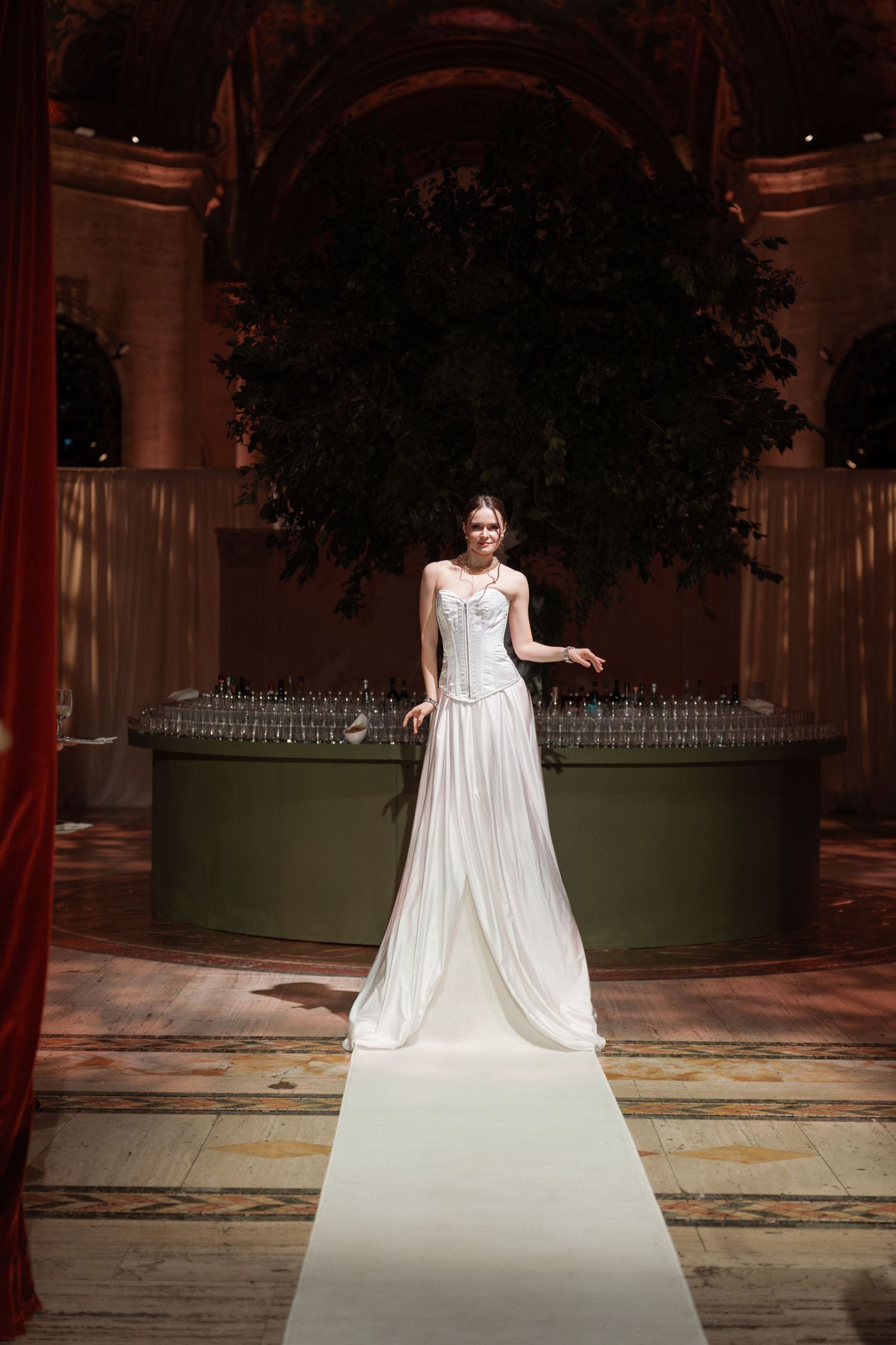 A woman in a long, flowing white wedding dress standing in a grand, ornate interior.