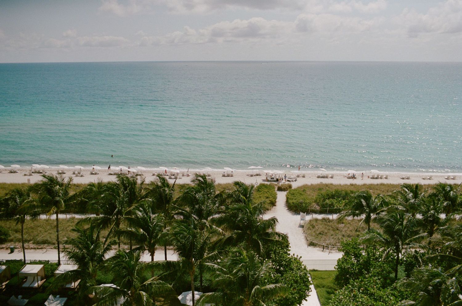 Panoramic aerial view of a beachfront resort with palm trees, white sand beach and turquoise ocean waters.