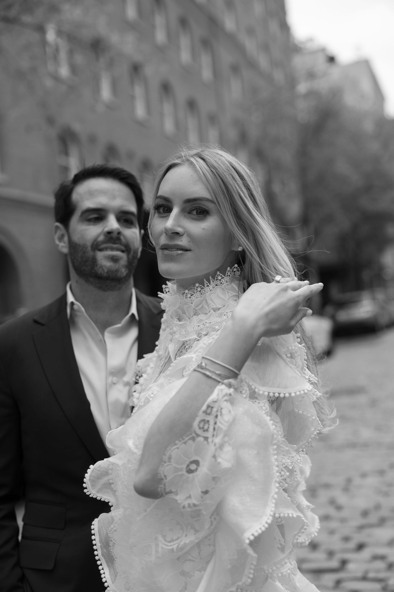 Elegant couple in formal wear posing on cobblestone street.