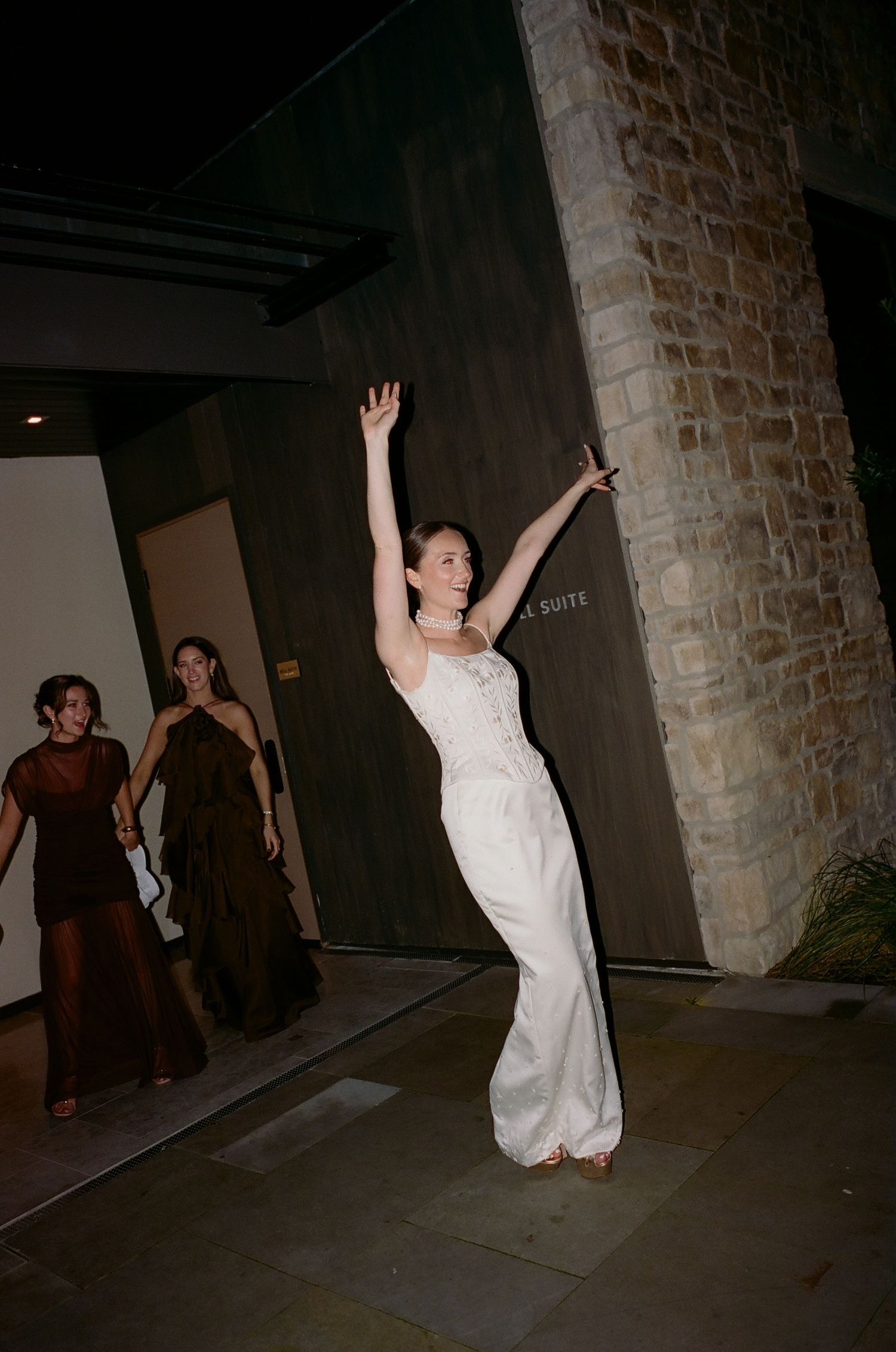 A person in a white dress dances joyfully with raised arms while others watch in formal attire.