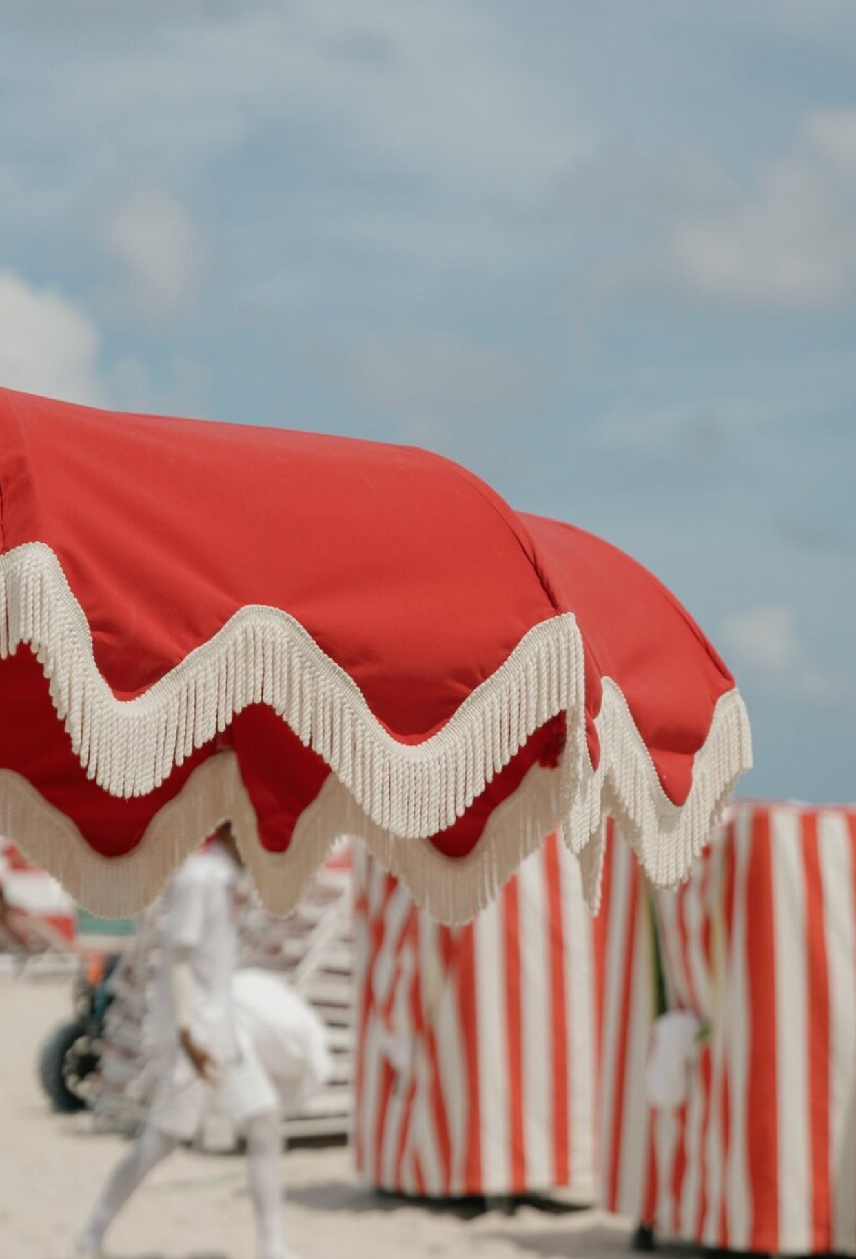 Red and white striped beach cabanas with decorative fringe on a sunny coastline.