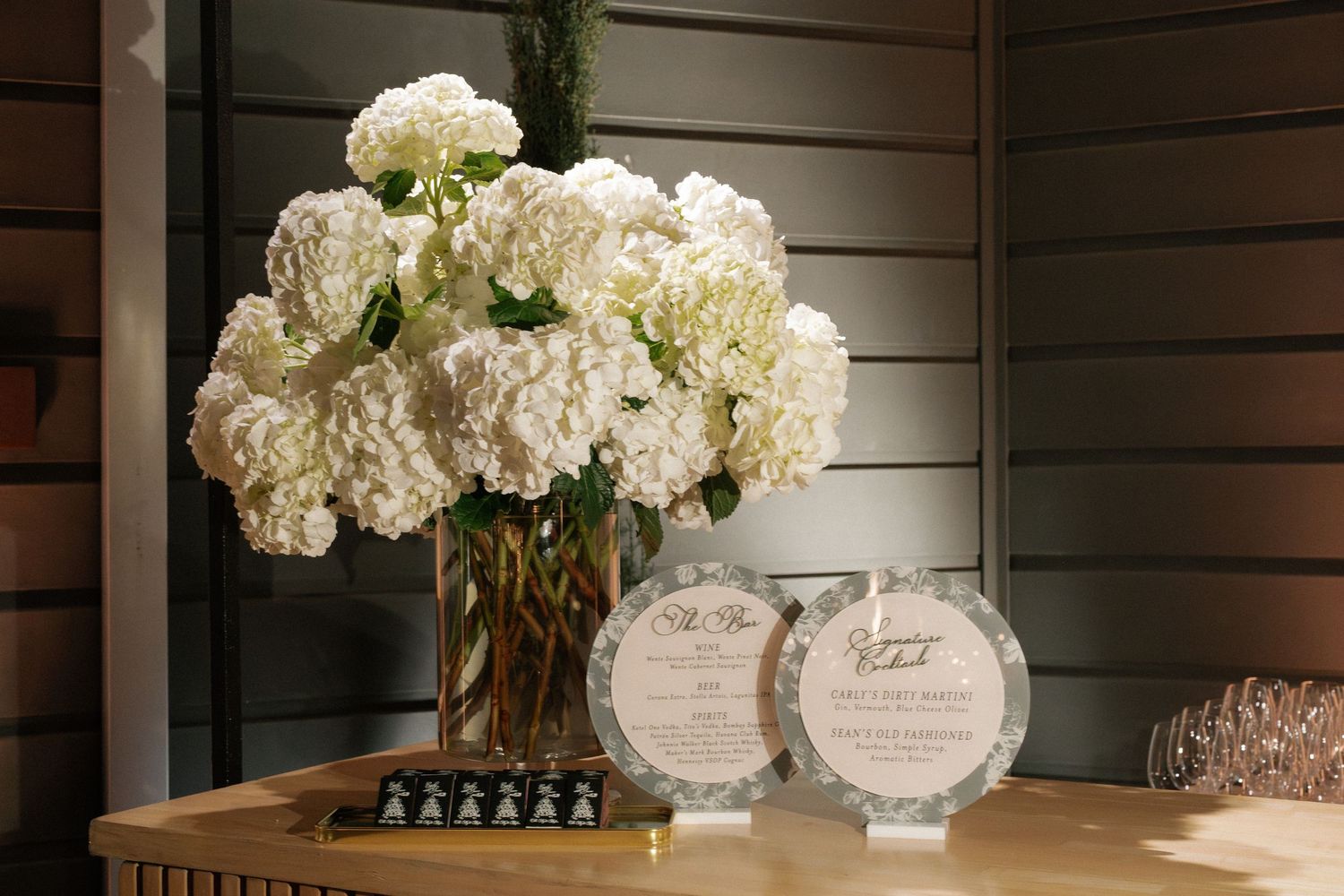 White hydrangea floral arrangements in crystal vases on wooden shelving.