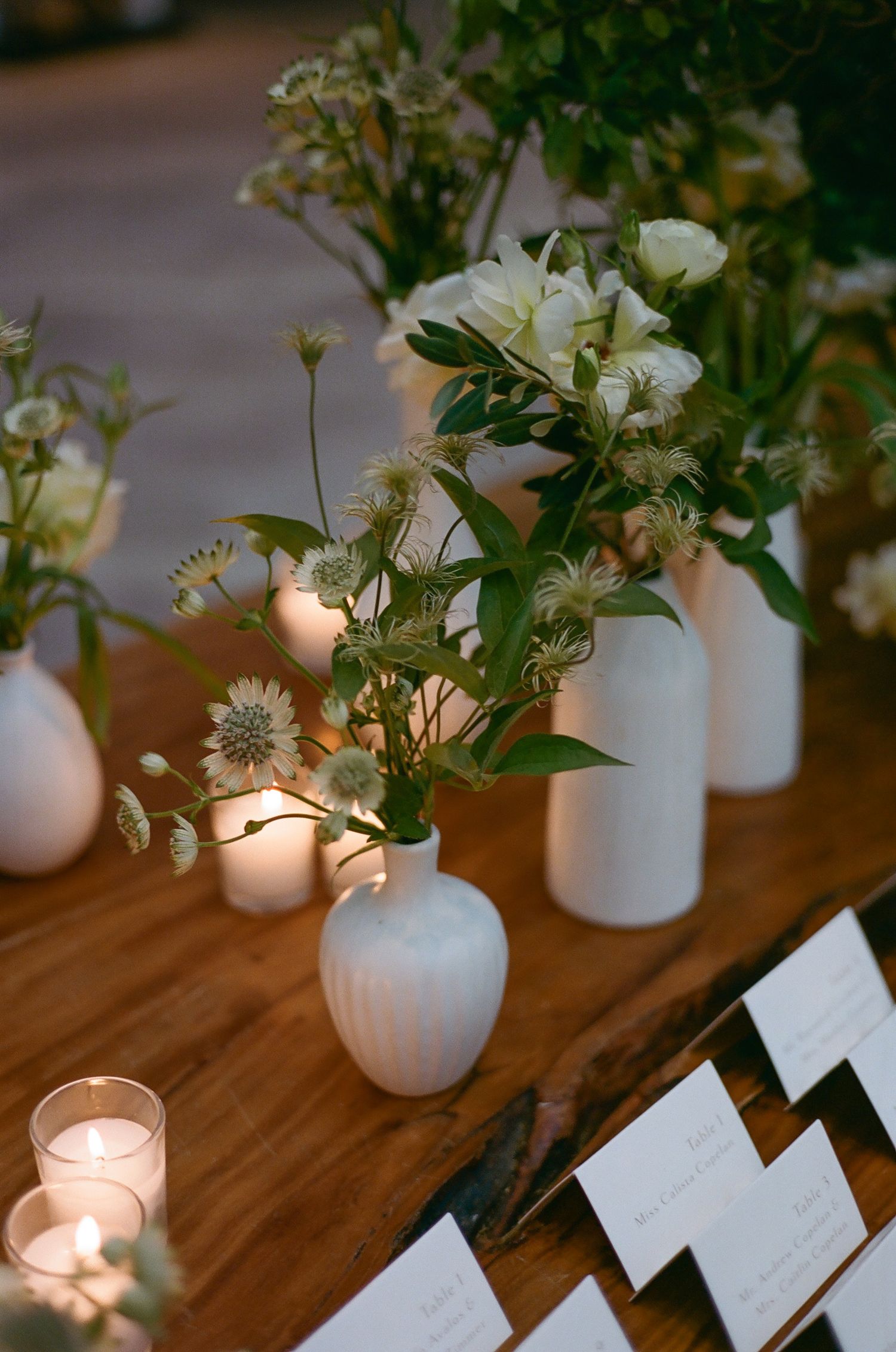 Elegant table settings with white floral centerpieces and glowing candles.