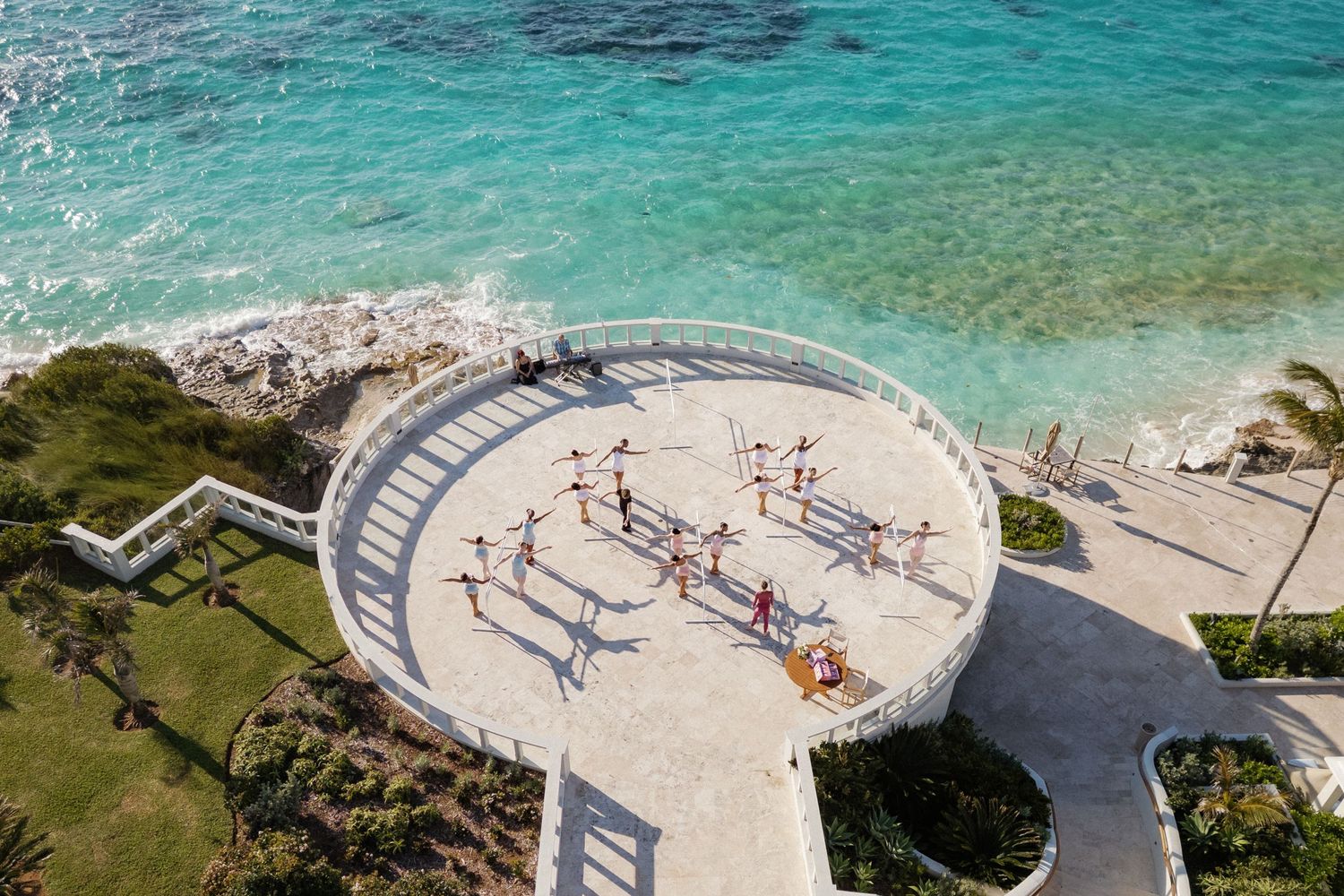 An aerial view of a circular structure with several people on it, surrounded by the clear blue ocean.