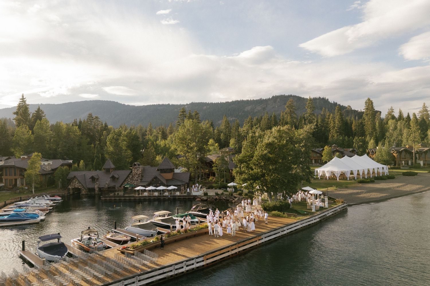 Panoramic view of lakeside venue with mountains and boats in background.
