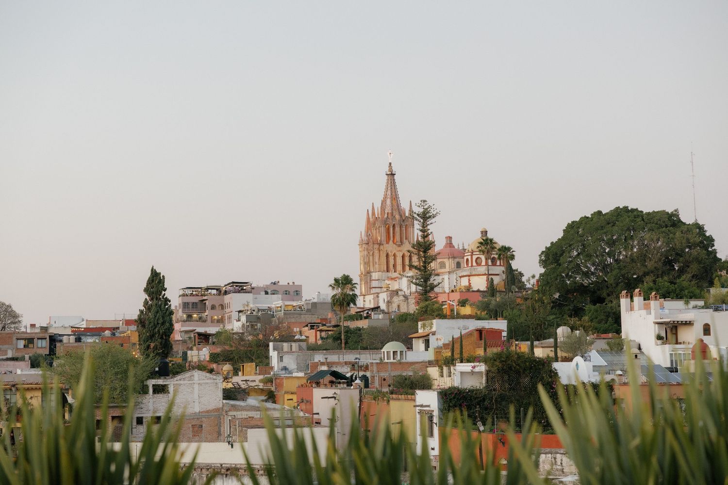 Panoramic cityscape view showing church spires and colonial architecture against a cloudy sky.
