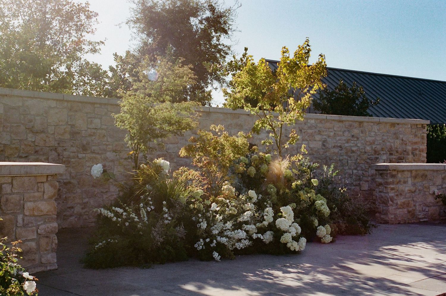 Stone wall and landscaping at an outdoor wedding venue under blue skies.