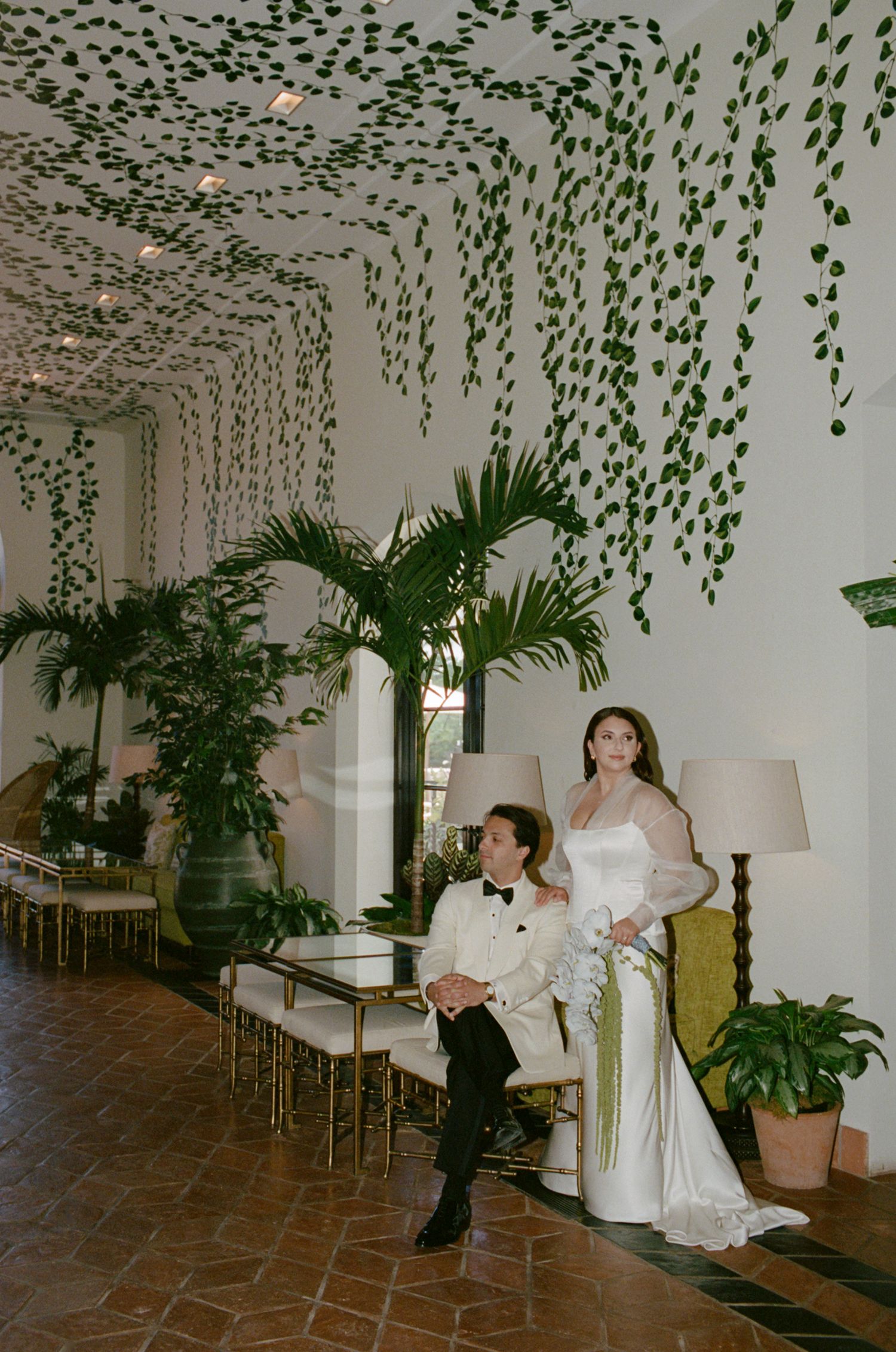 Wedding venue decorated with hanging greenery and tropical plants on tiled floors.