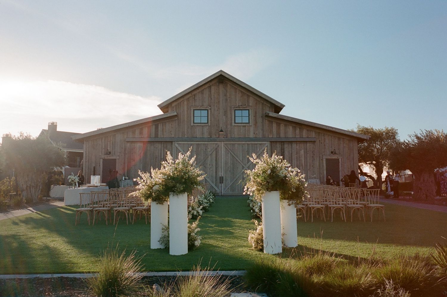 Rustic barn venue exterior with floral arch during golden hour.