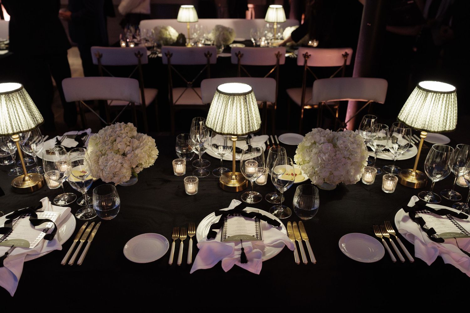 Elegant wedding reception tables set with white lampshades and dark tablecloths creating intimate ambiance.