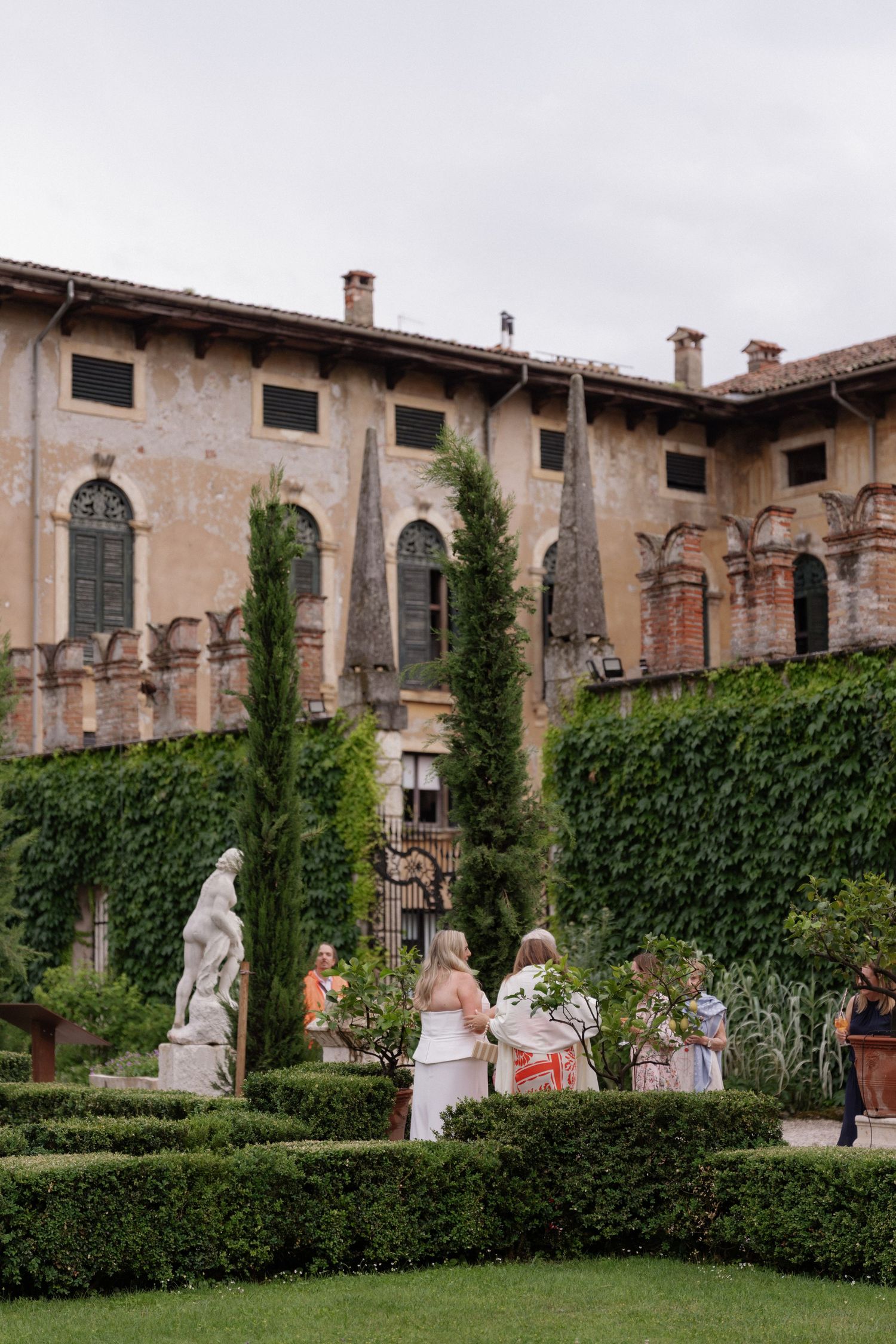 Elegant garden wedding at historic Italian villa with sculpted hedges, classical statues, and ivy-covered stone walls.