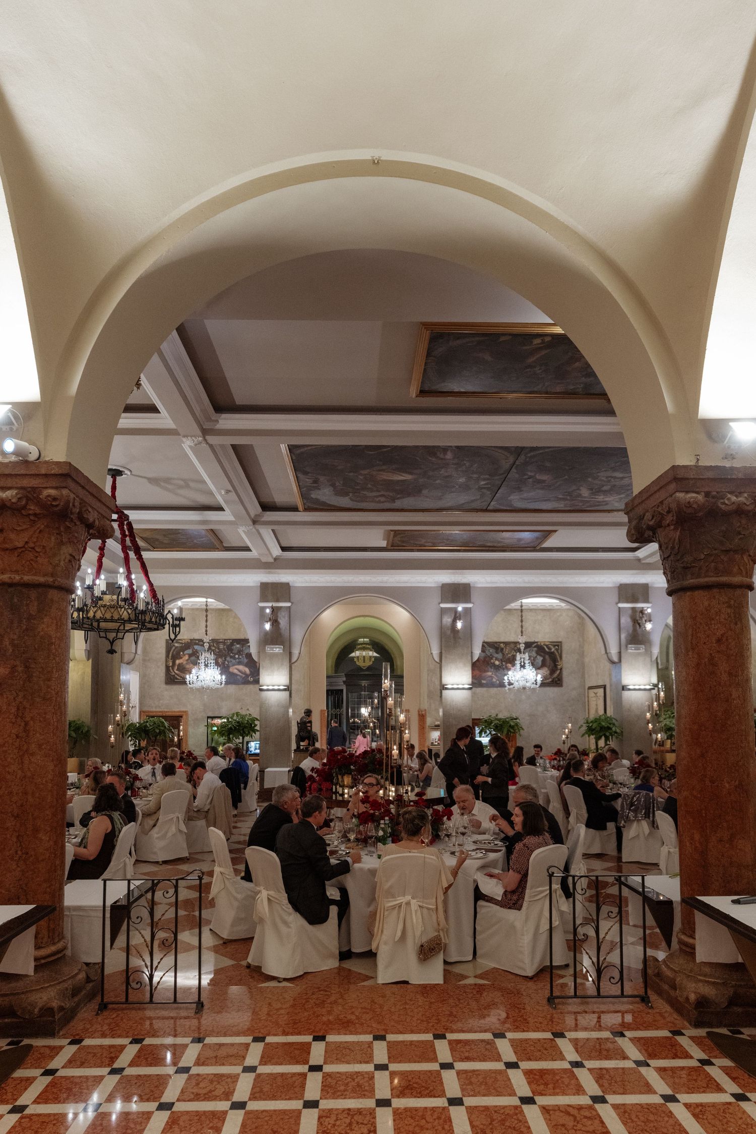 Grand wedding reception banquet hall with marble columns, arched ceilings, and guests dining at decorated tables.