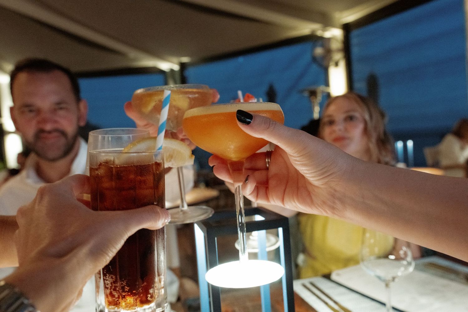 People toasting drinks at a bar or restaurant in the evening.
