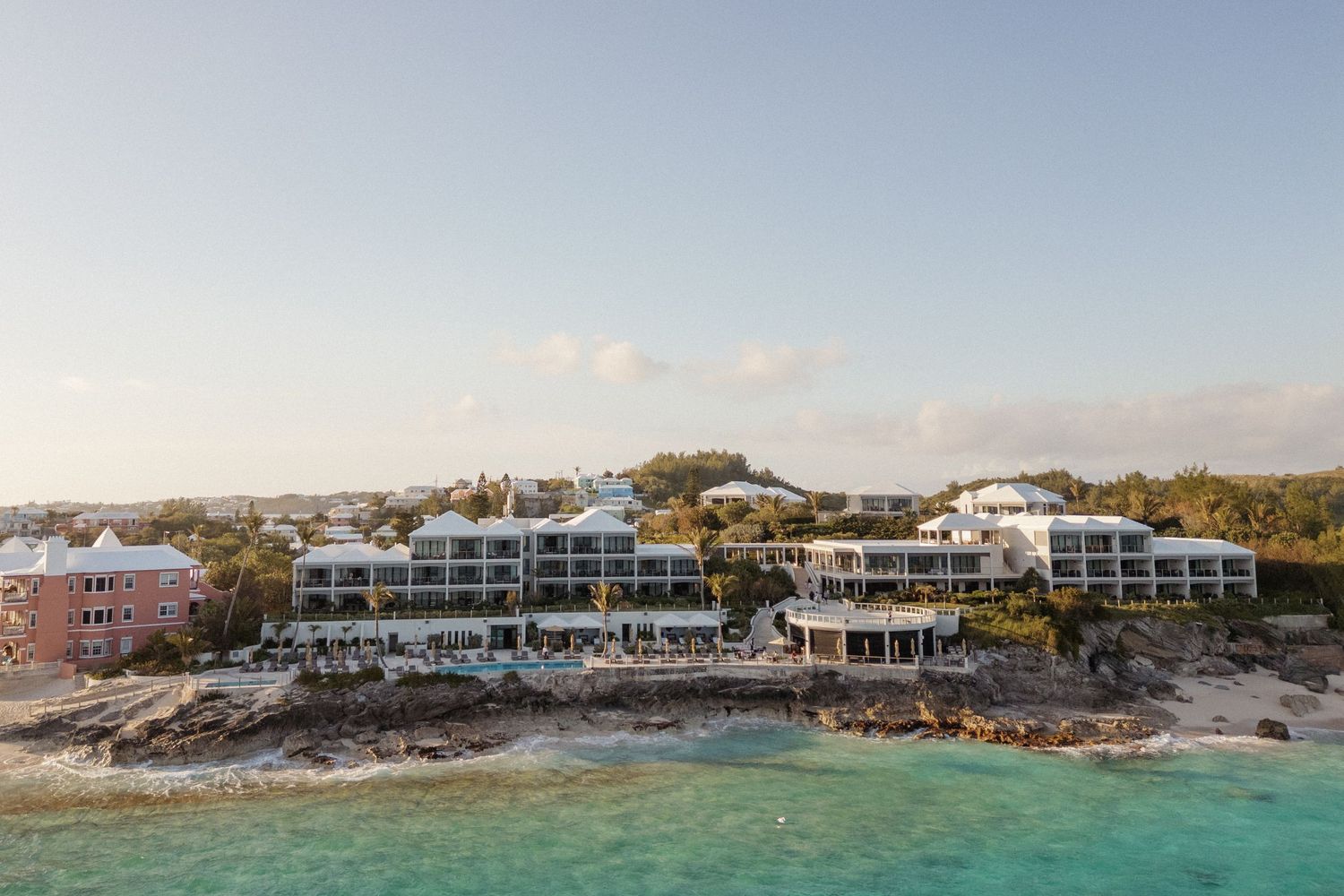 This image shows a coastal resort with multi-story buildings overlooking the ocean, surrounded by lush vegetation.