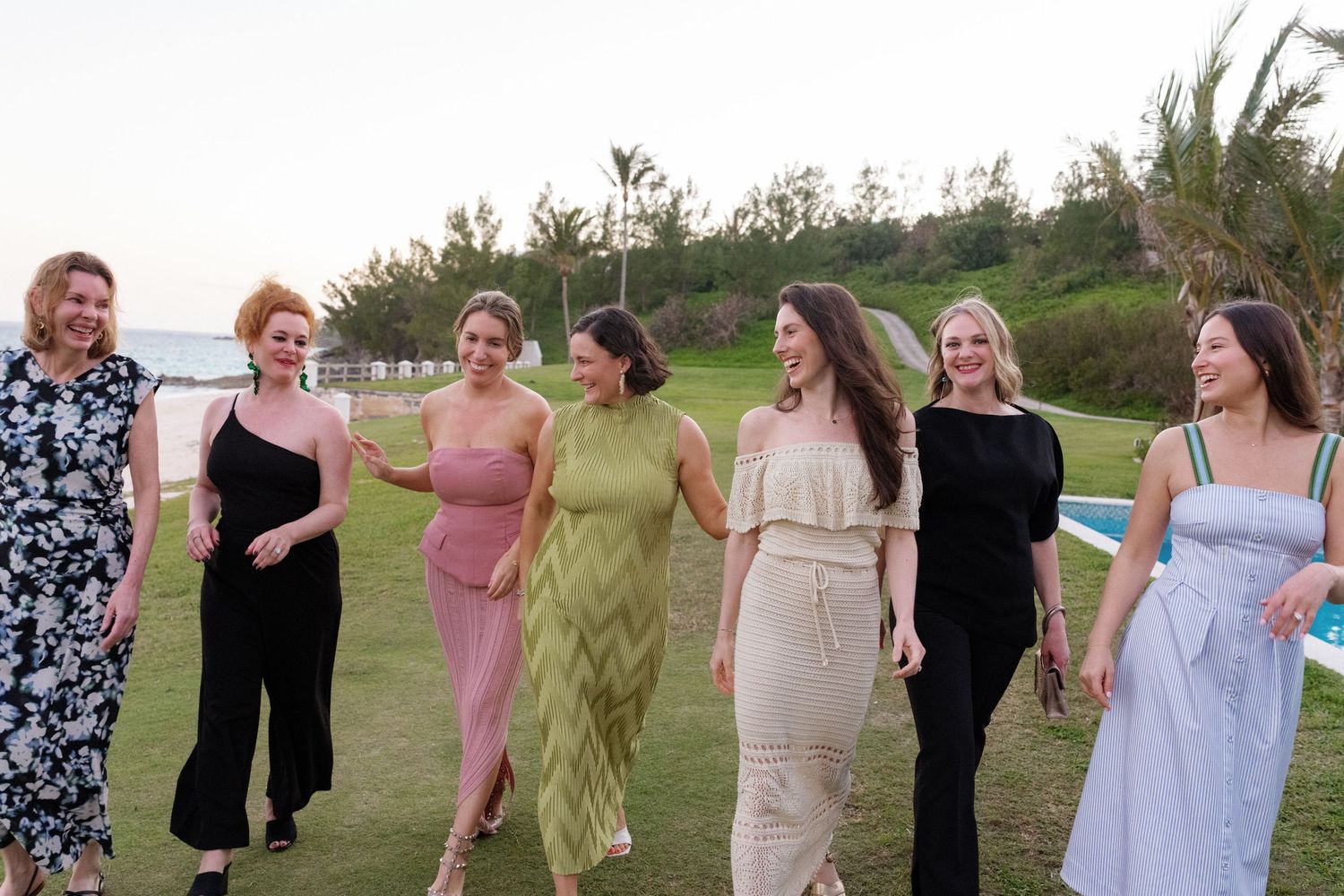 A group of women wearing formal dresses of various colors standing outdoors on a grassy field.