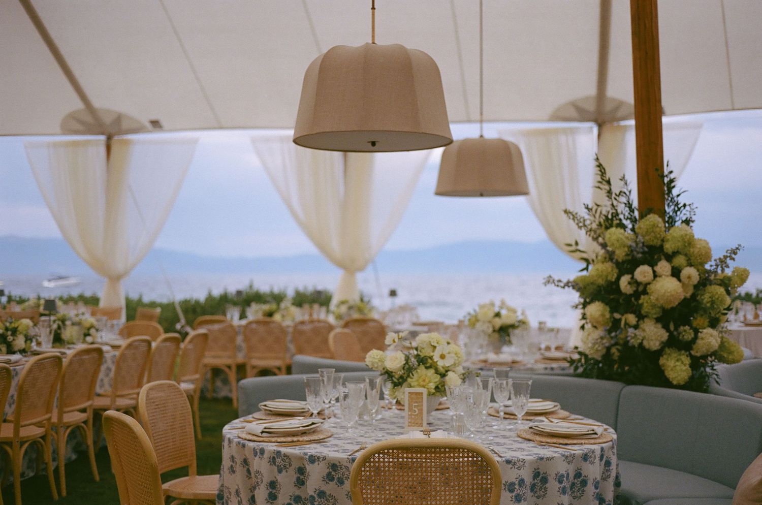 Elegant wedding reception setup with white drapes, floral centerpieces and rattan chairs.