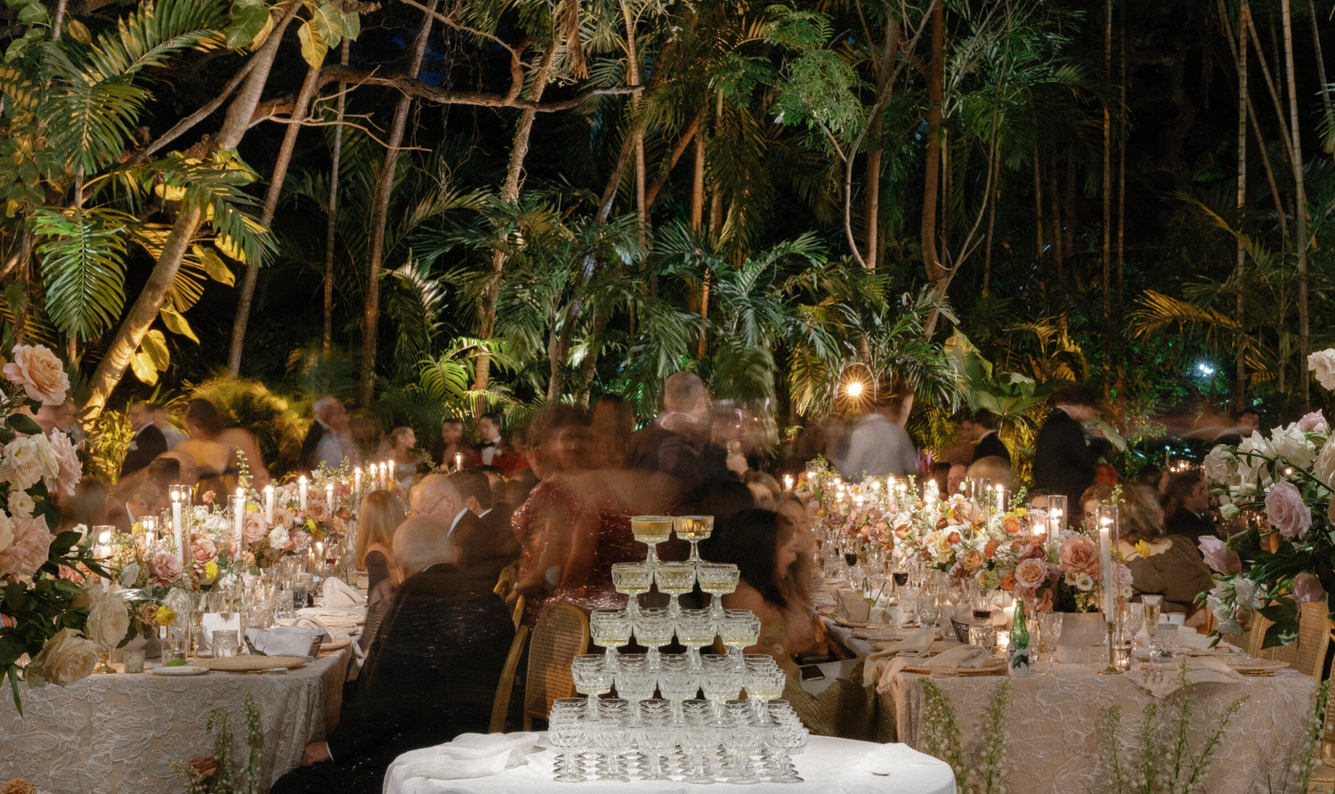 Elegant wedding reception table setup with champagne tower and floral arrangements in garden setting.