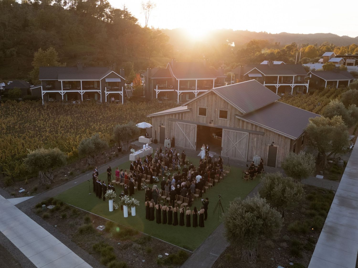 Aerial view of an outdoor wedding venue at sunset with guests gathered on the lawn.