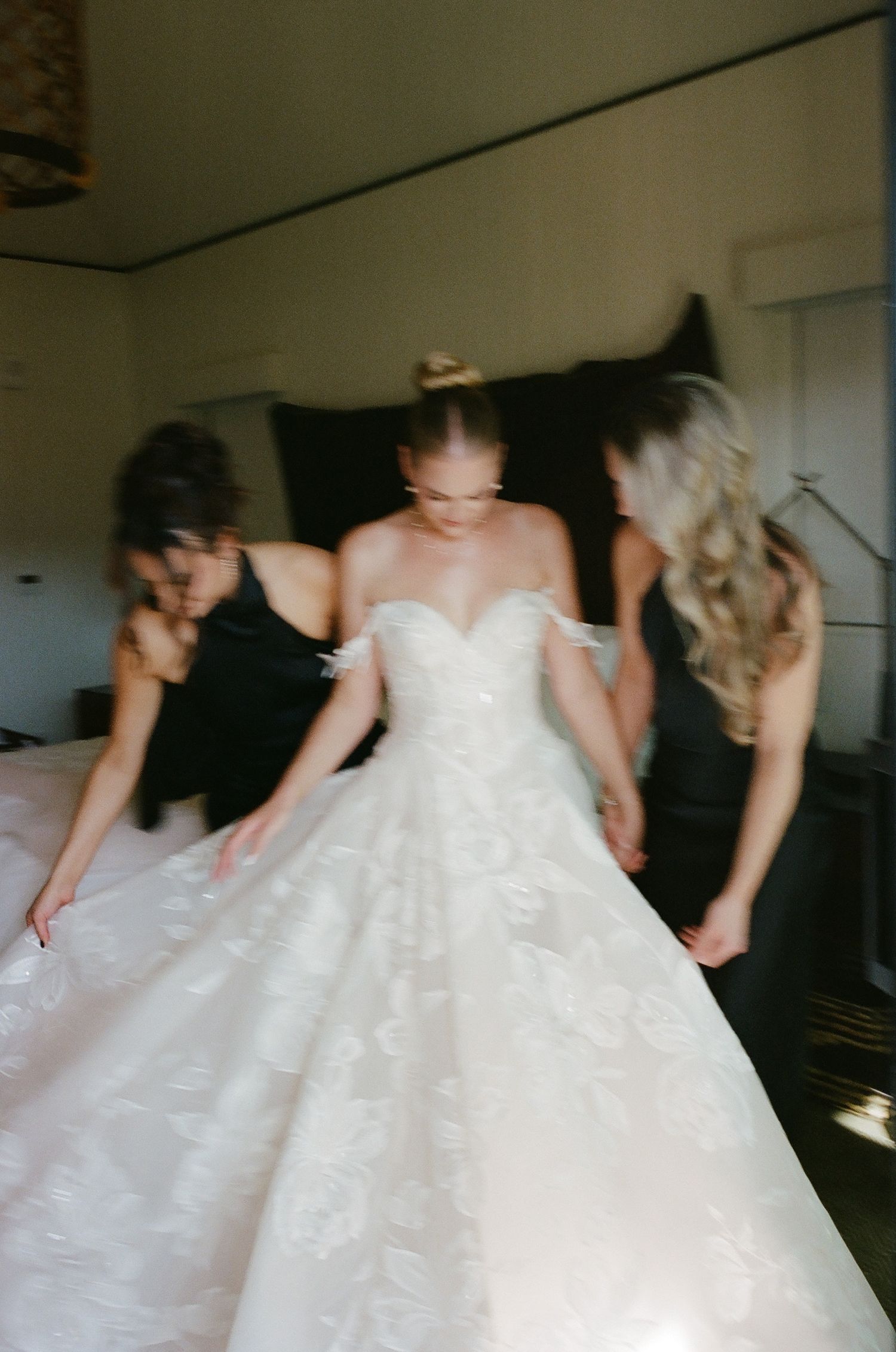 Motion-blurred image of people helping with a wedding dress fitting.
