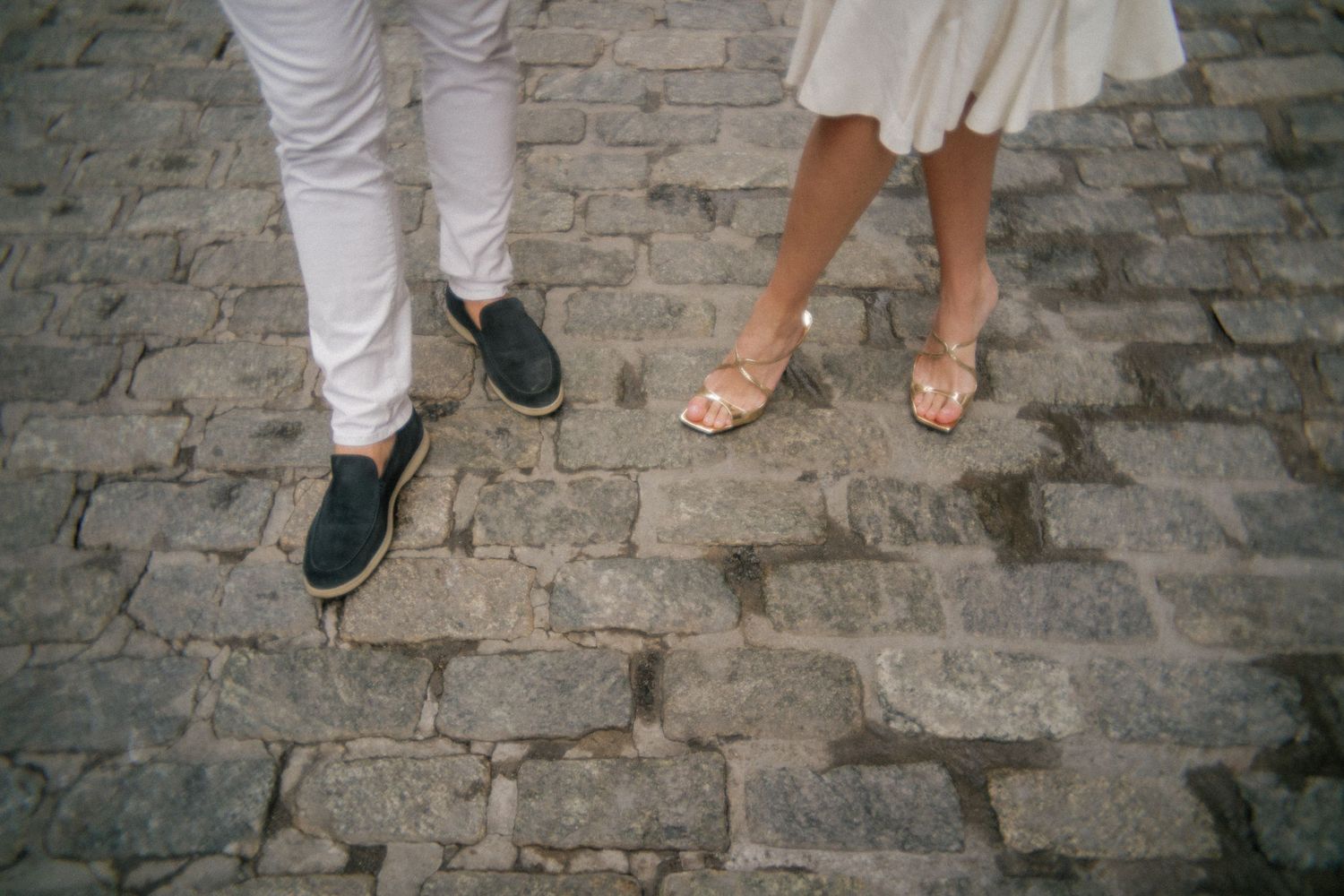 Detail shot of feet and legs walking on cobblestone street in formal wear.