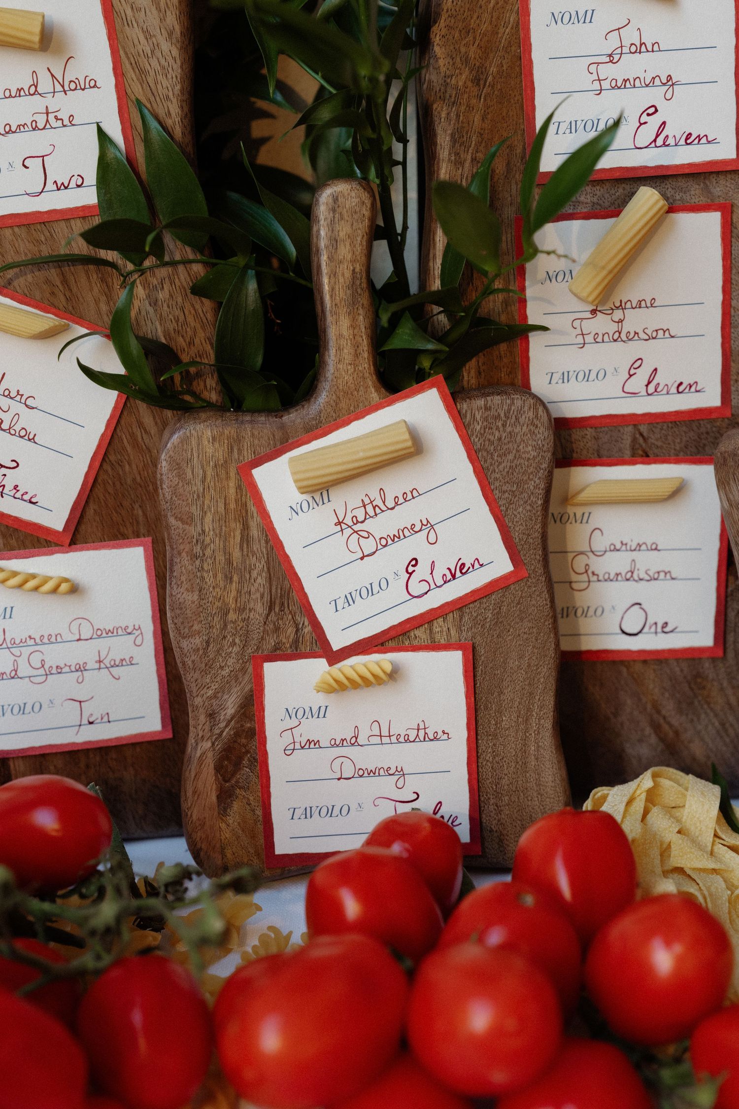 Rustic Italian wedding seating cards with pasta accents on wooden boards surrounded by fresh red tomatoes.