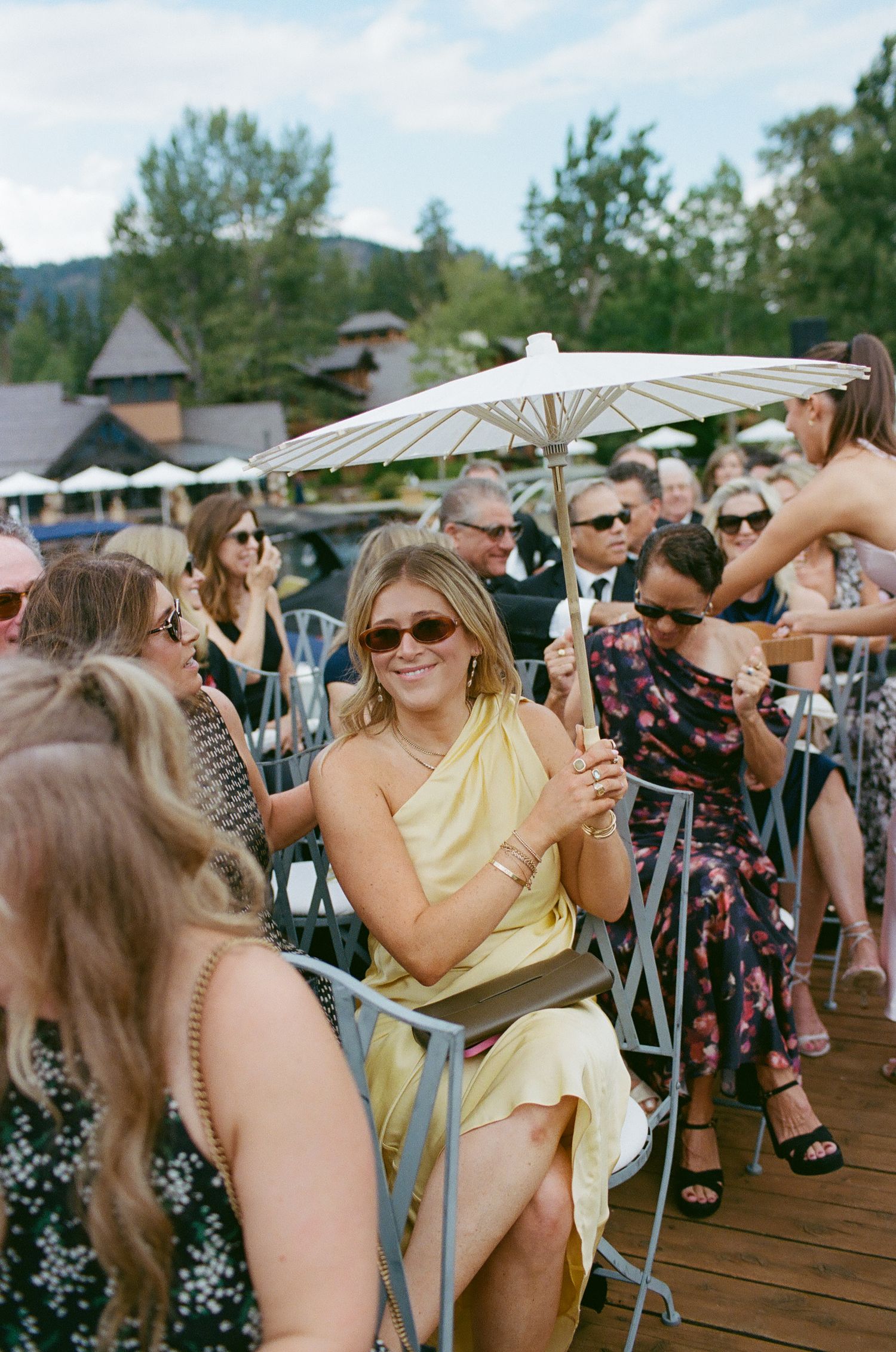 Wedding guests enjoying an outdoor celebration with parasols on a sunny deck.