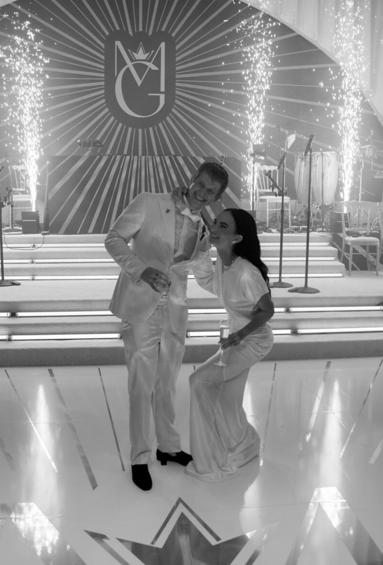 Elegant couple dancing on illuminated dance floor with sparklers and art deco style backdrop.