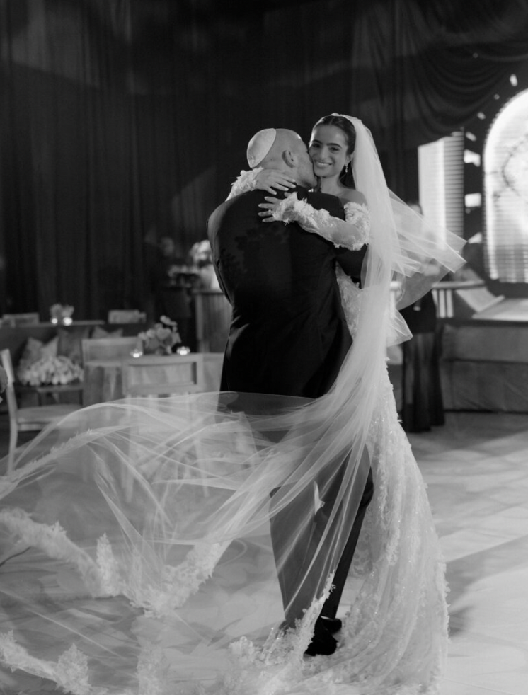 Black and white photo of a couple sharing their first dance with flowing veil movement.