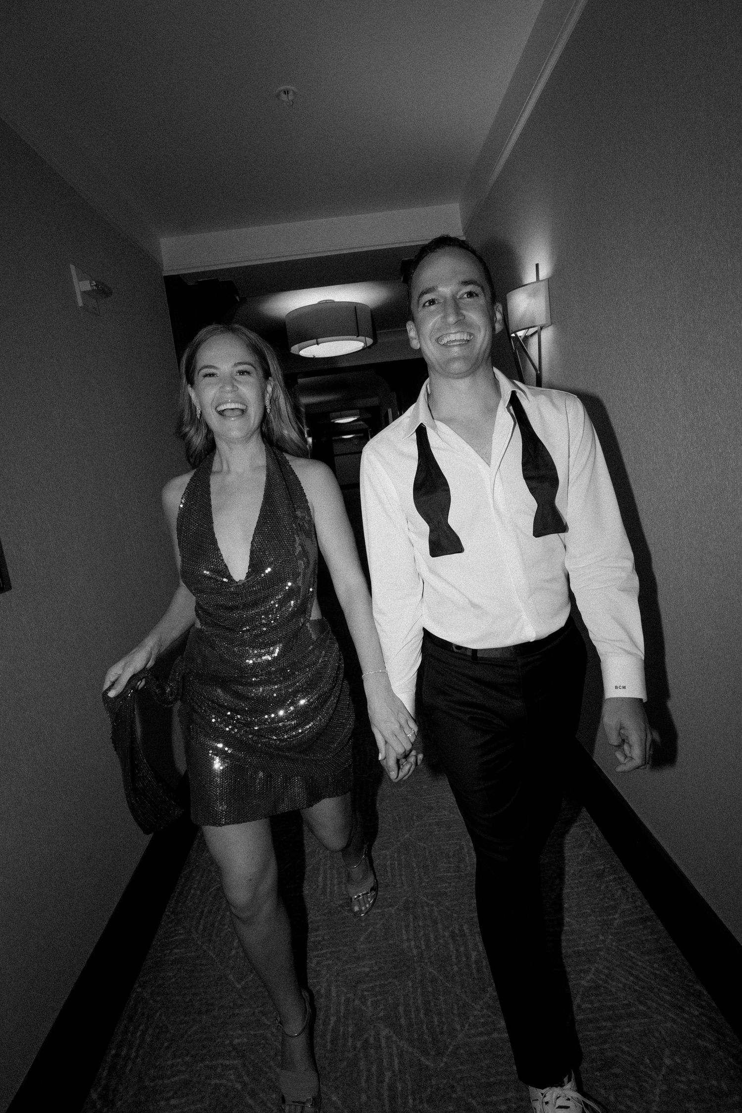 Black and white photo of guests dancing in a hotel hallway during wedding festivities.