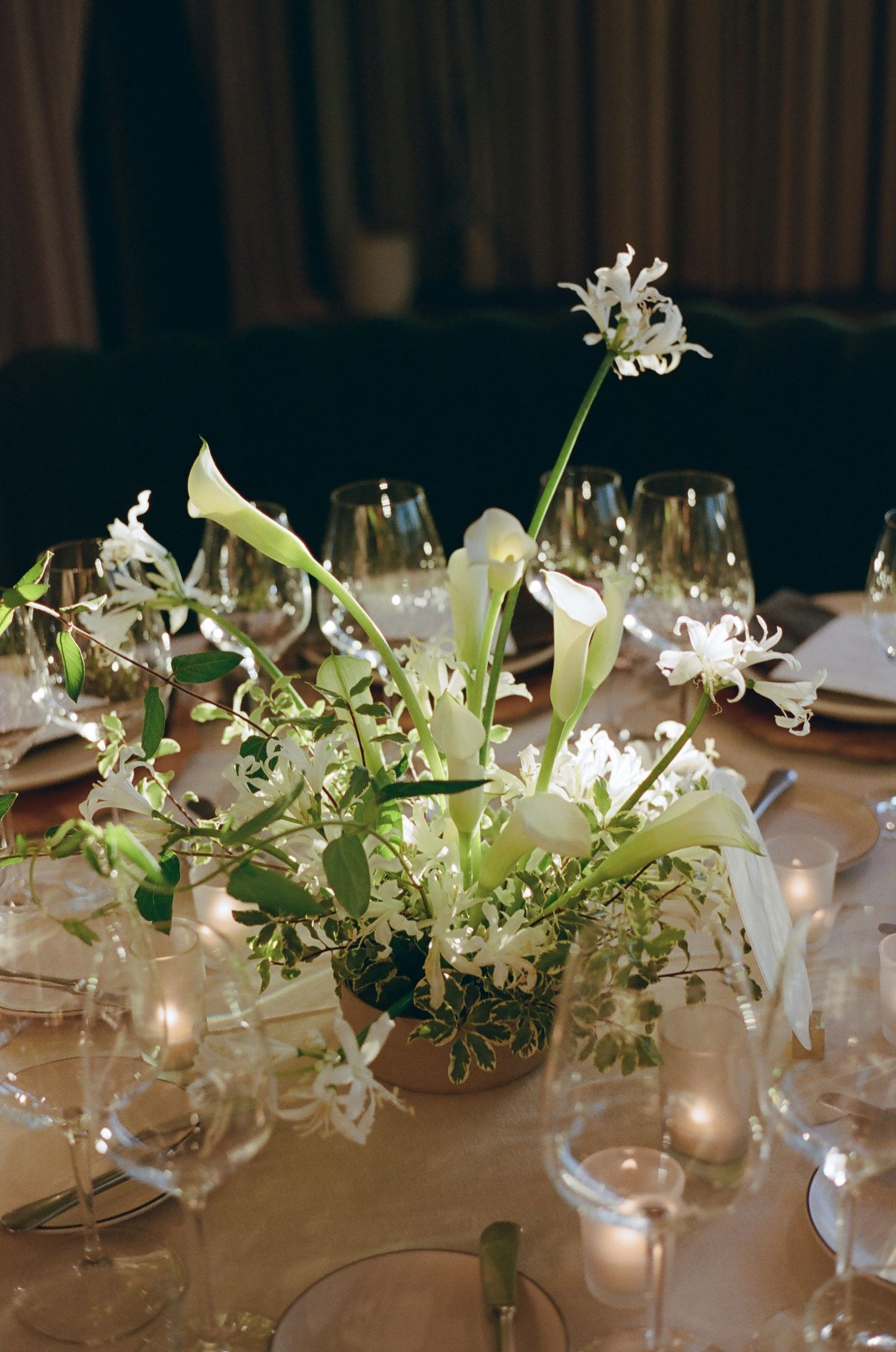 Elegant white floral centerpieces with lilies and greenery on reception tables.