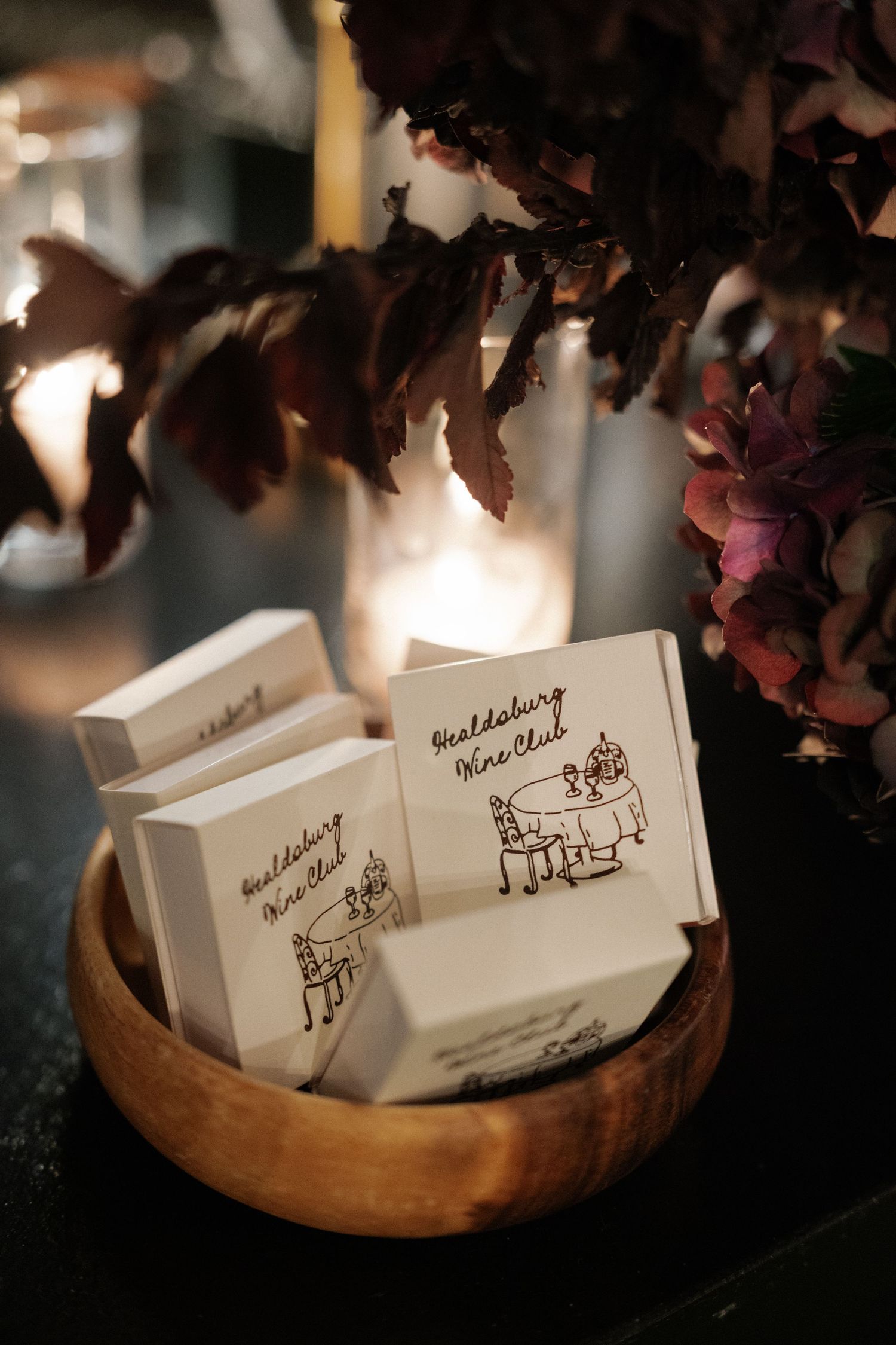 Wedding place cards with hand-drawn illustrations displayed in a wooden bowl.