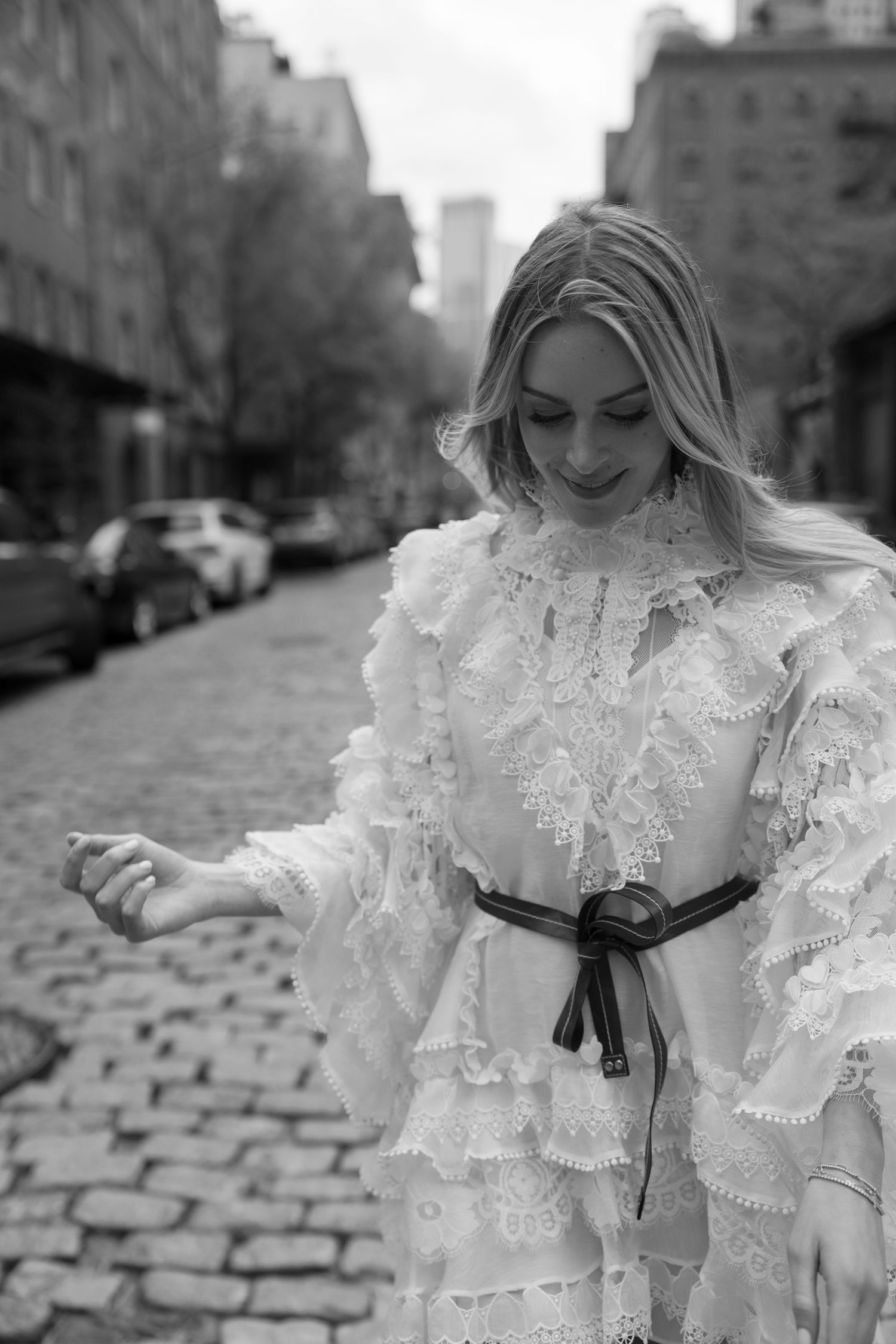 A detailed view of an intricate white lace dress with ruffles against an urban backdrop.