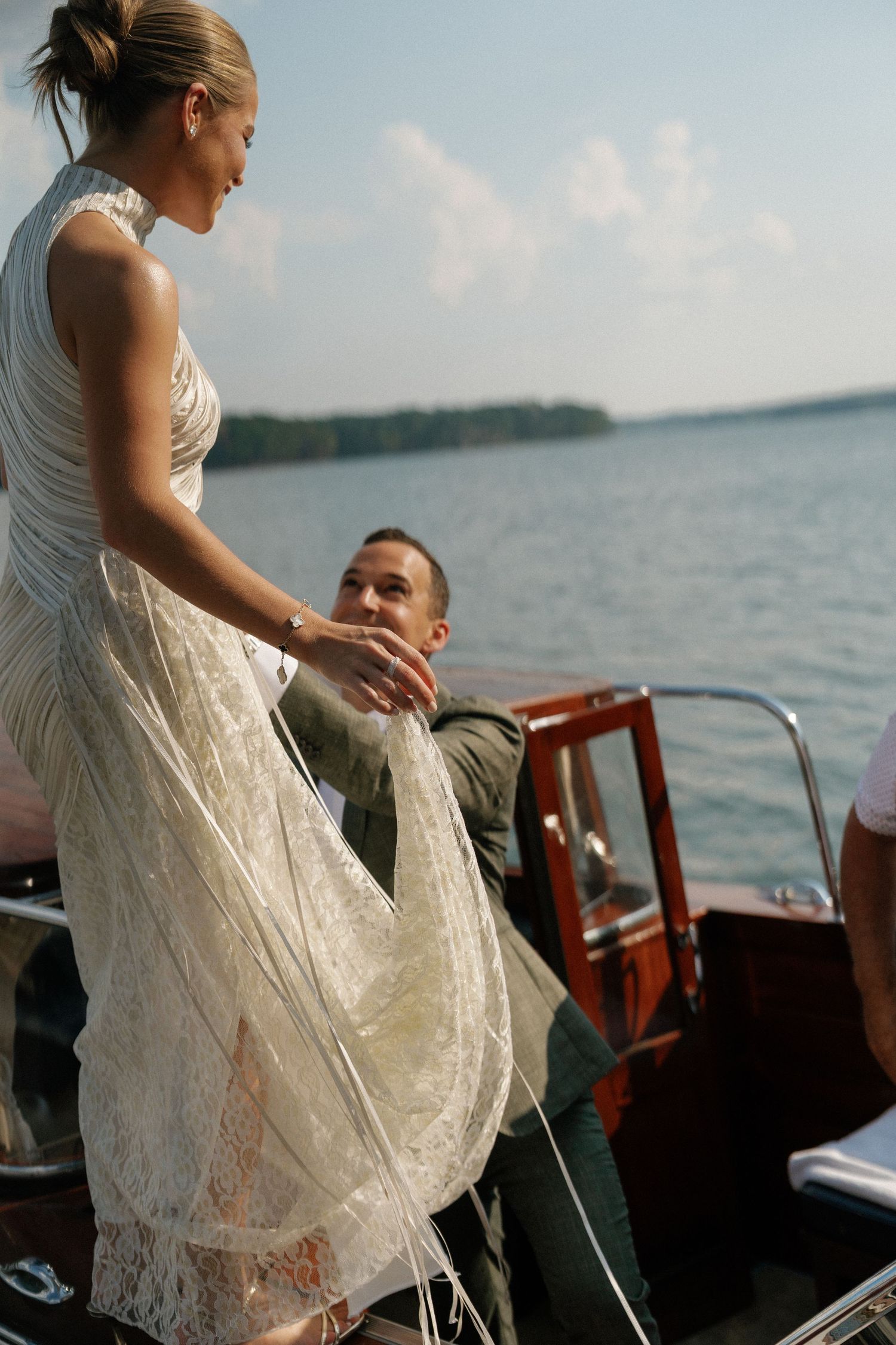 White lace dress flowing over the side of a wooden boat on calm waters.