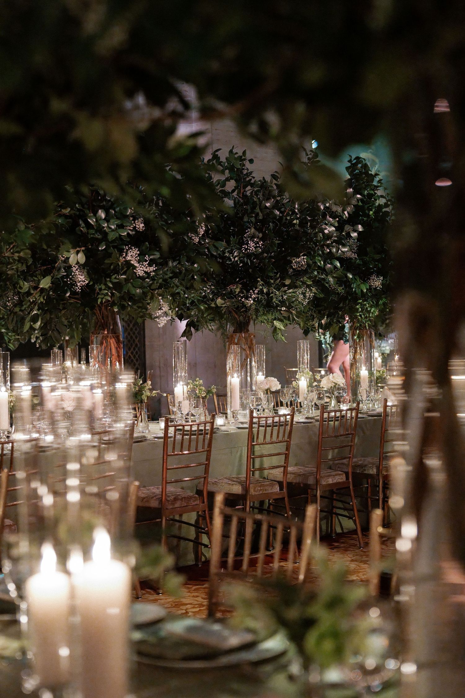 An elegant wedding reception setup with a lush floral arch and candles illuminating the table settings.