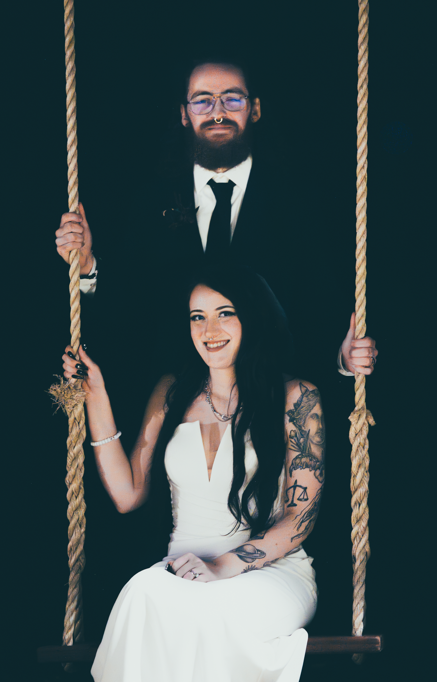 Couple posing playfully on rope swings in formal wedding attire.