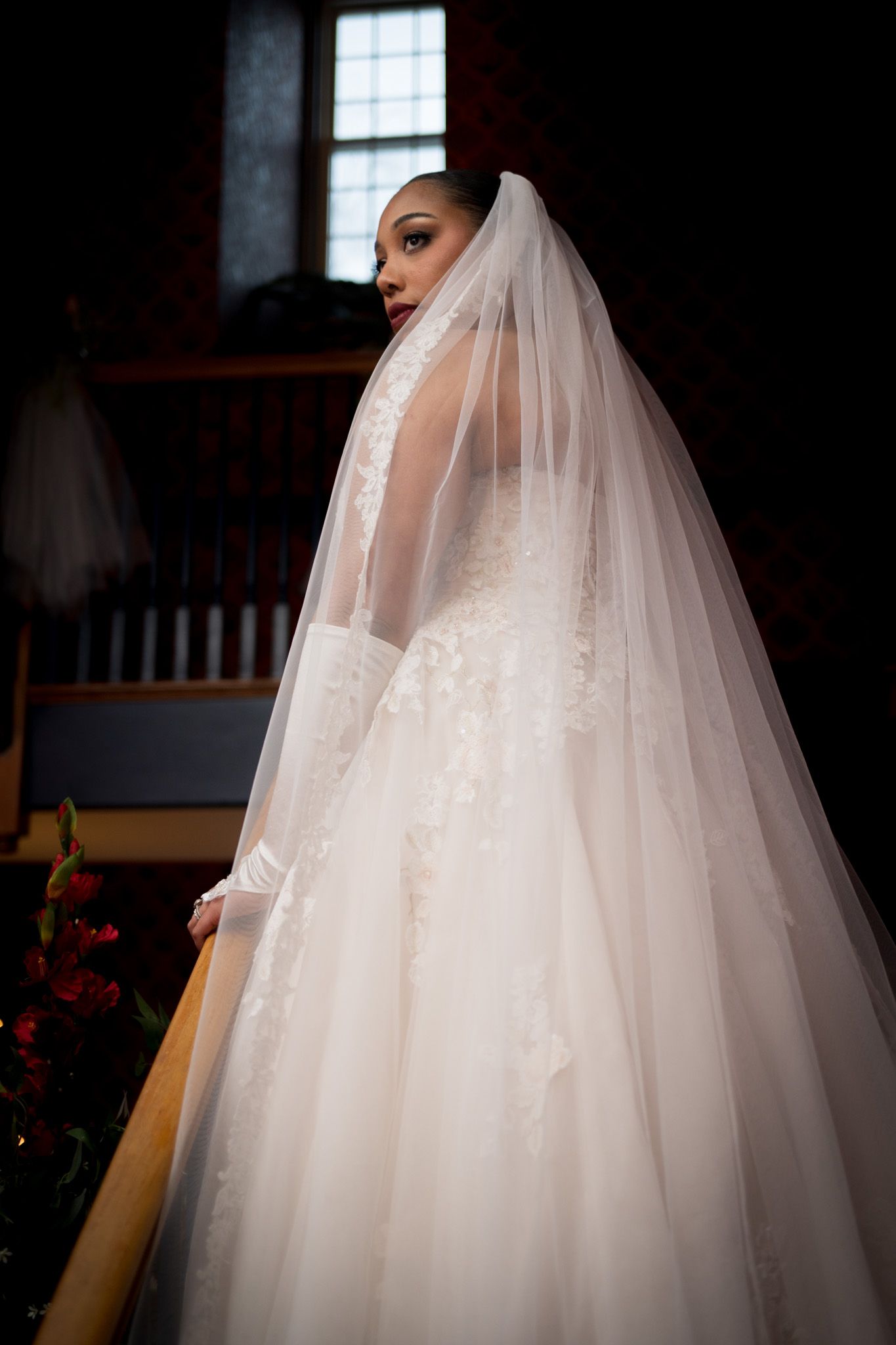 Elegant wedding dress with flowing veil captured in dramatic window light.