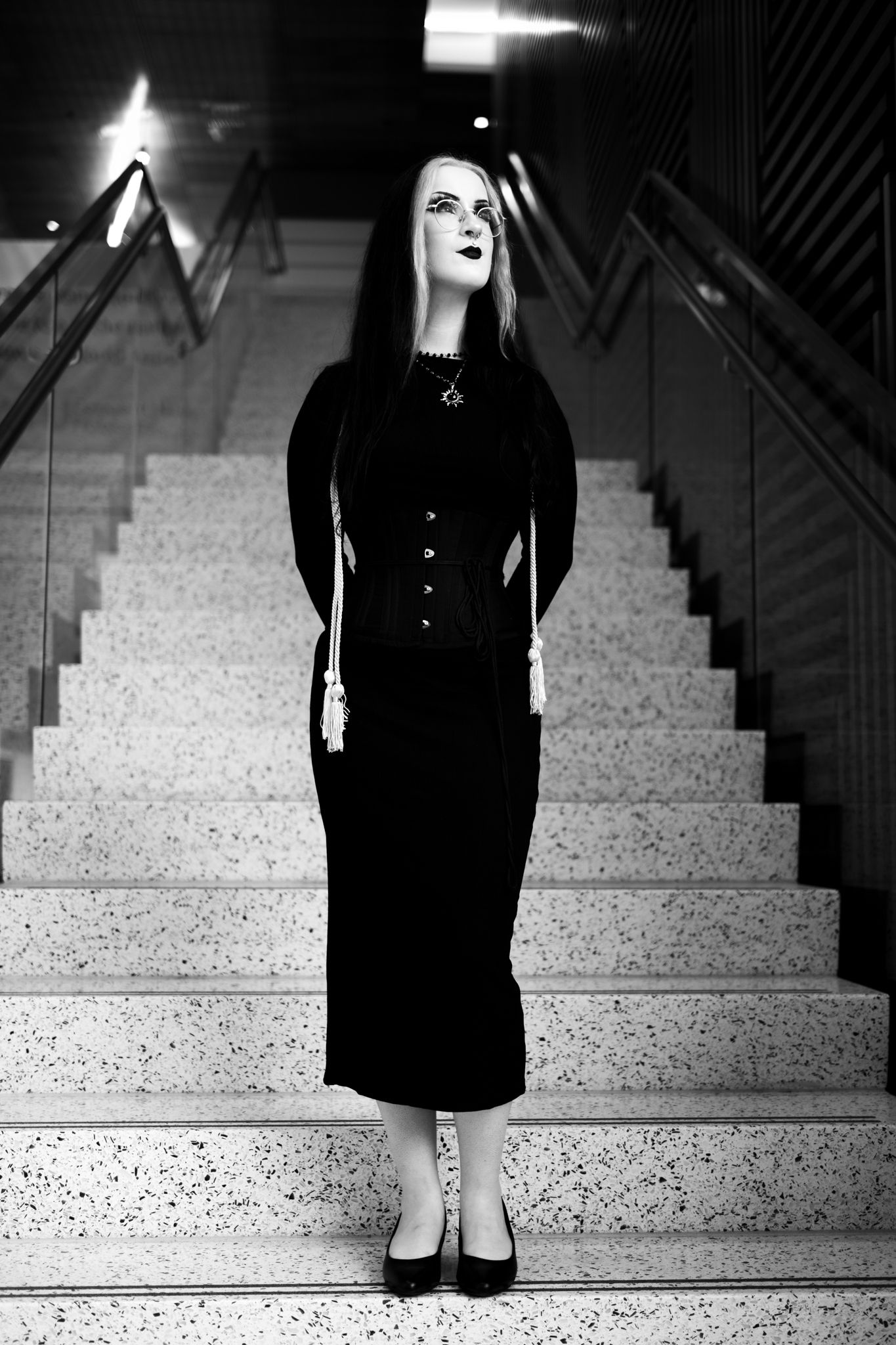 Person in black dress standing on concrete stairs in high contrast black and white.